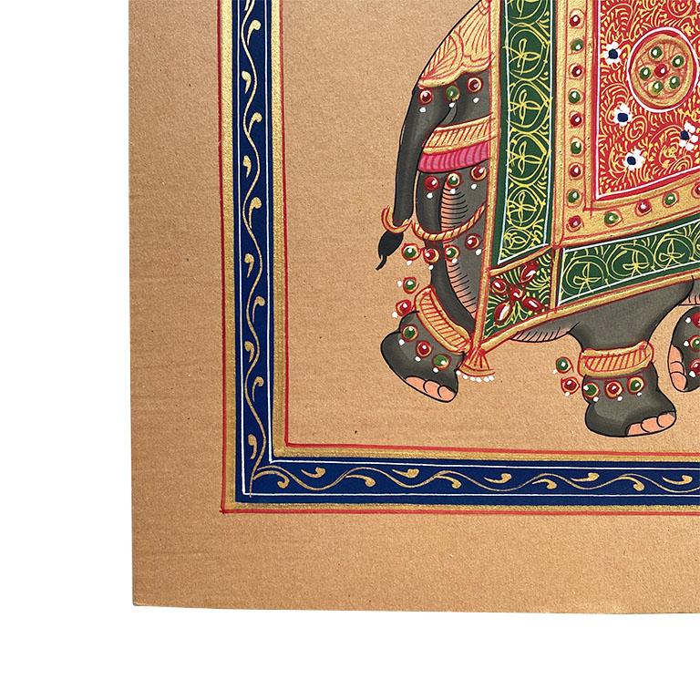 A beautiful hand painted portrait of an elephant in full Indian wedding regalia. The animal is shown mid-stride and is covered in a green, red, and gold cloth. A blue and gold stylized border surrounds the piece. All on a brown background.