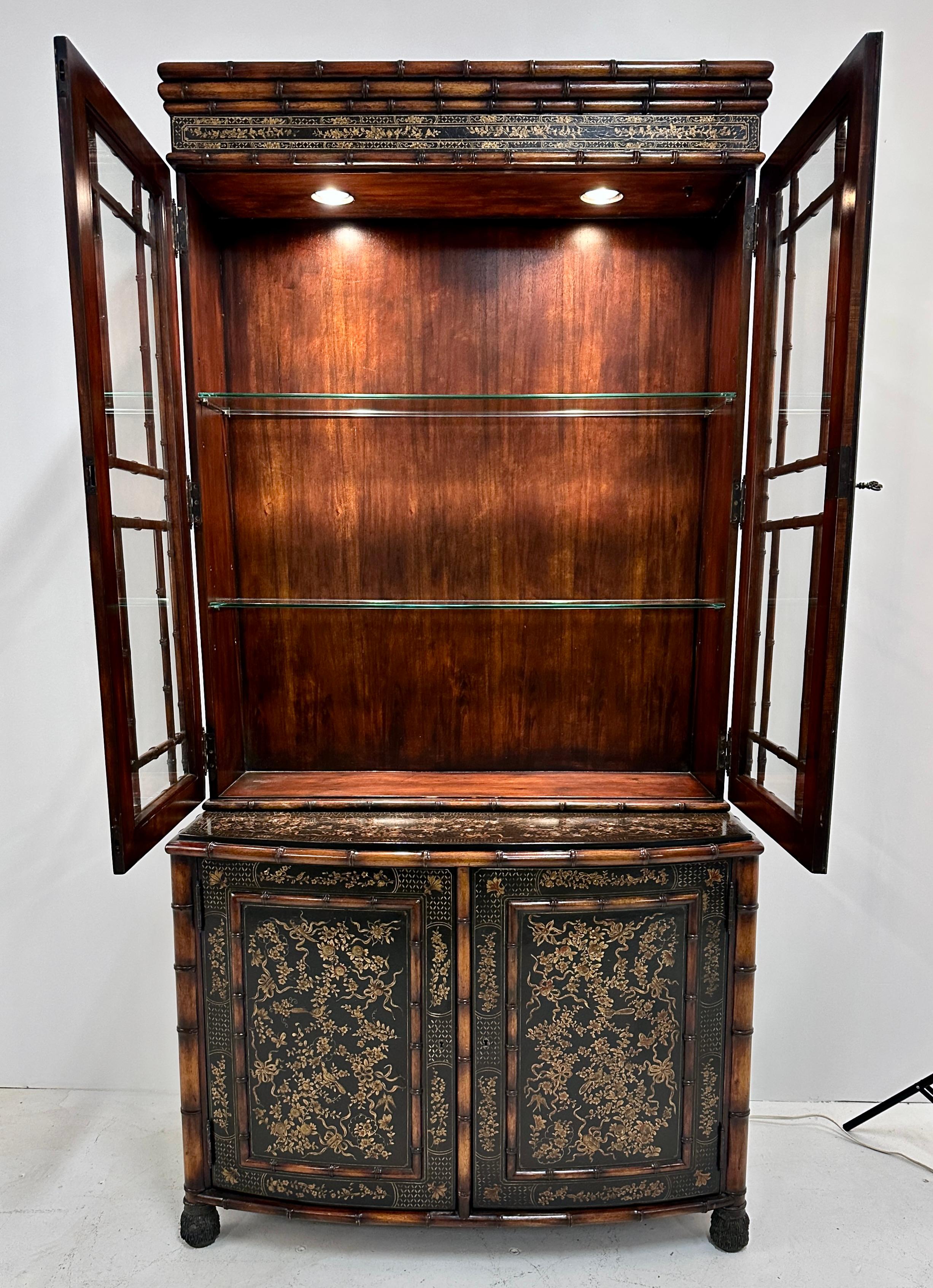 A lovely cabinet with hand painted decoration in gold over a very dark green, detailed with faux bamboo trimming. The upper section behind mullioned glass doors has glass shelves and integrated down lights. The lower cabinet features a single wood