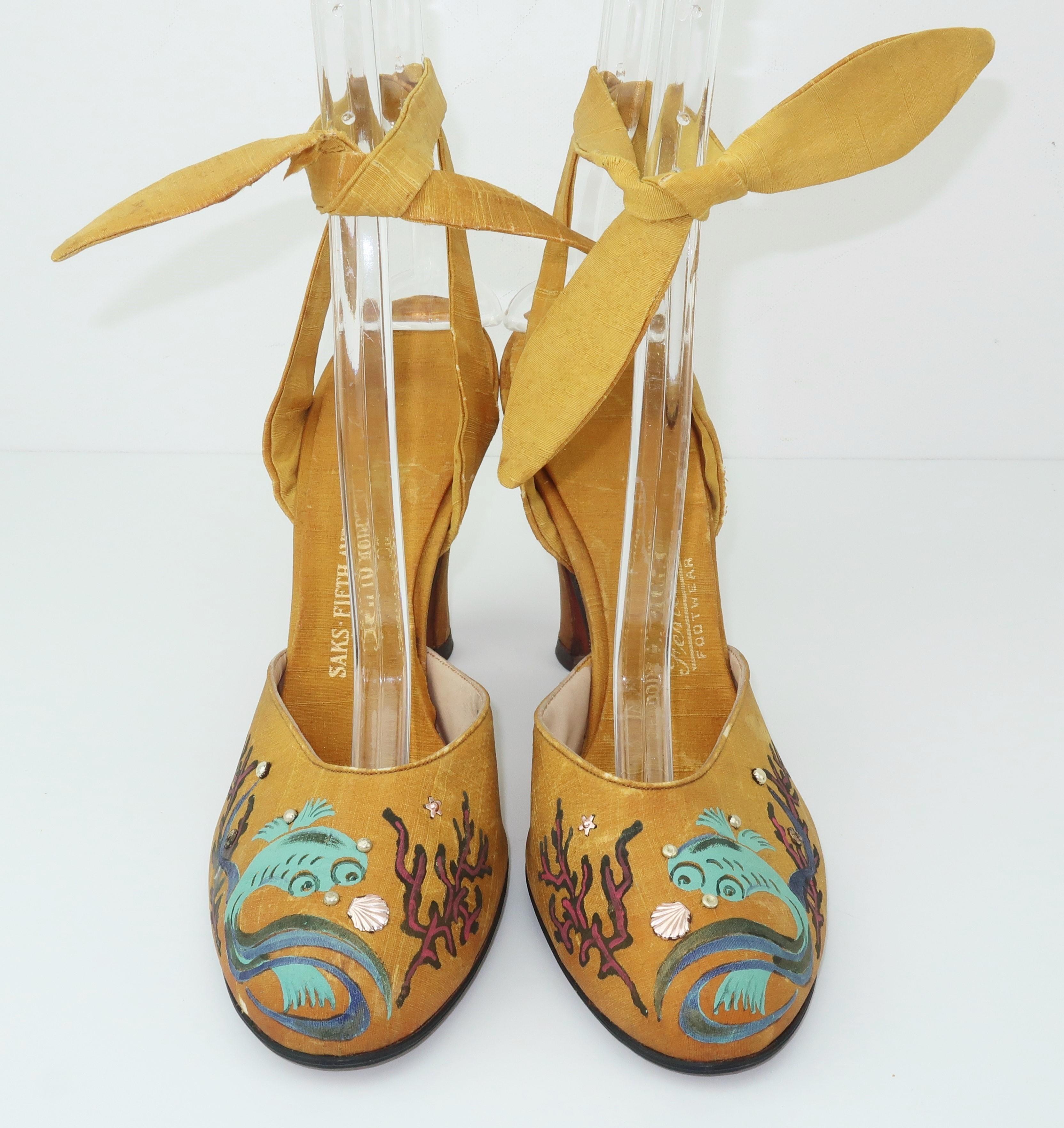 Made by Fenton for Saks Fifth Avenue, these 1930's golden yellow silk ankle strap shoes are exquisite pieces of art depicting whimsical hand painted imagery of sea life including an aqua fish and red coral tinged in gold.  The art work is accented