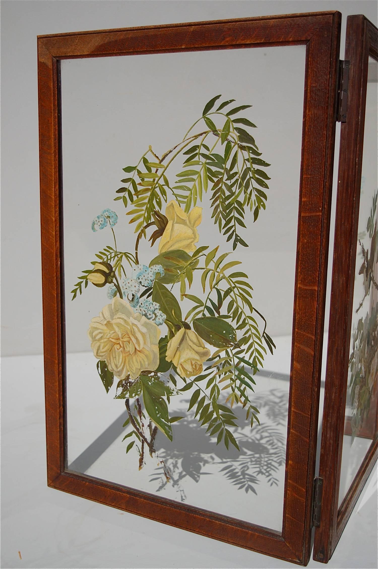 A folding screen made from four glass panels, set in an oak wooden frame. Each panel features a hand-painted still life decoration on one side of the glass depicting wild flowers or birds. The panels are connected with metal hinges, so that the