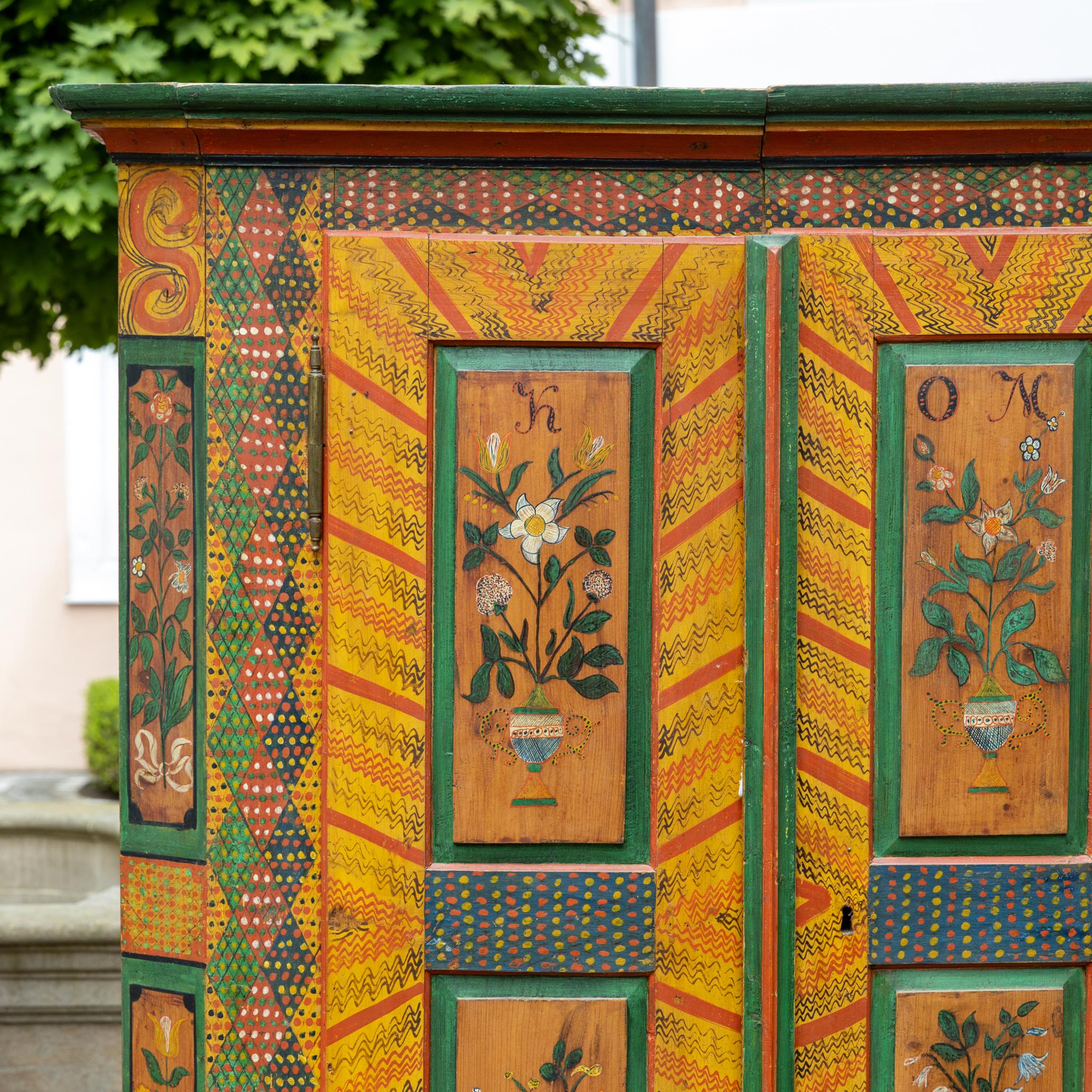 Straordinario armadio a due ante di arte popolare con vivaci decorazioni floreali e geometriche. I pannelli delle porte sono ornati da vasi di fiori dipinti, circondati da bande e motivi a puntini in colori vivaci. Sulla barra inferiore e sulle
