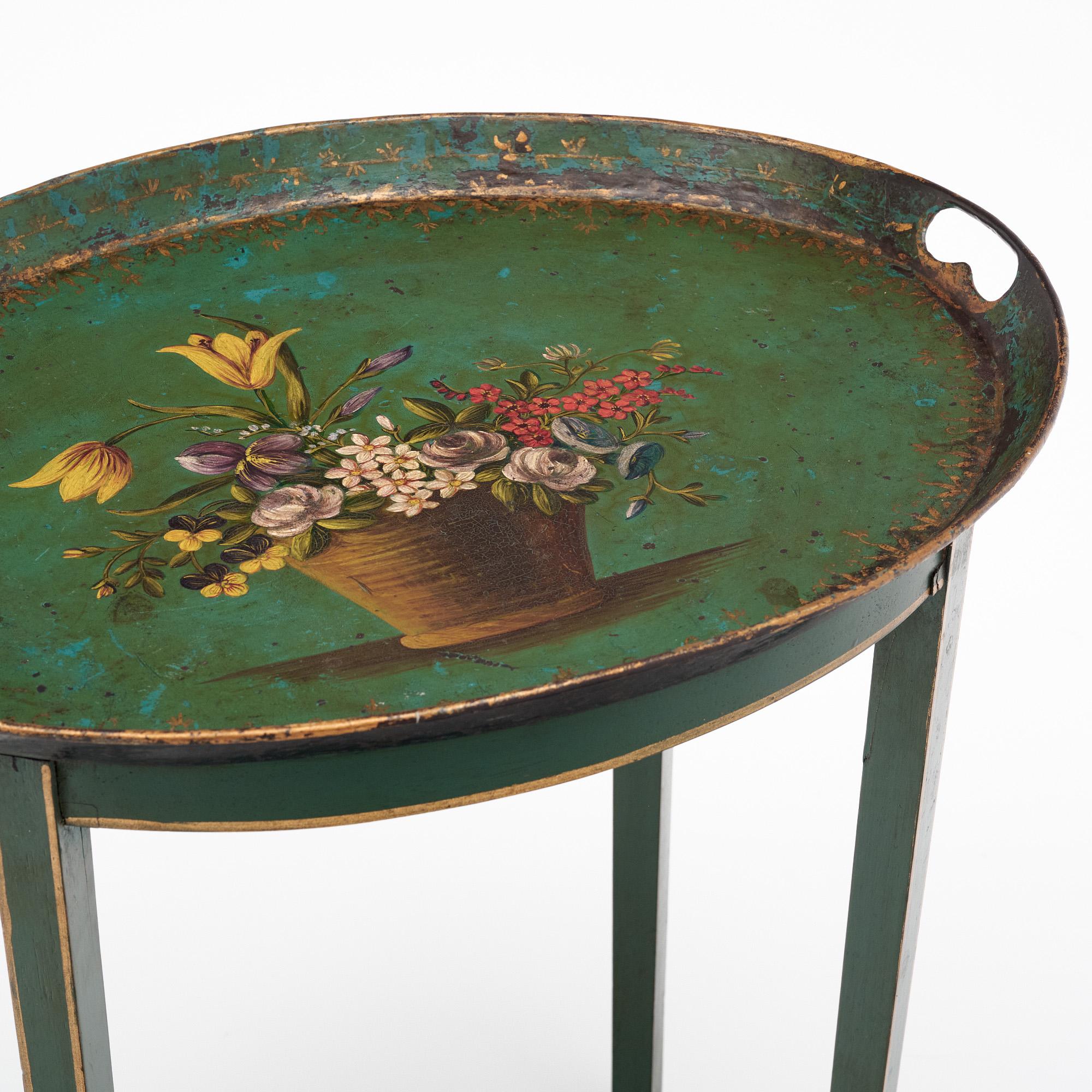 Delicate side table from France made of featuring a polychrome hand-painted finish in a primarily emerald green tone. There is a lovely patina over the entire piece. Gold leafing trims the legs and edges, while a striking floral still-life decorates
