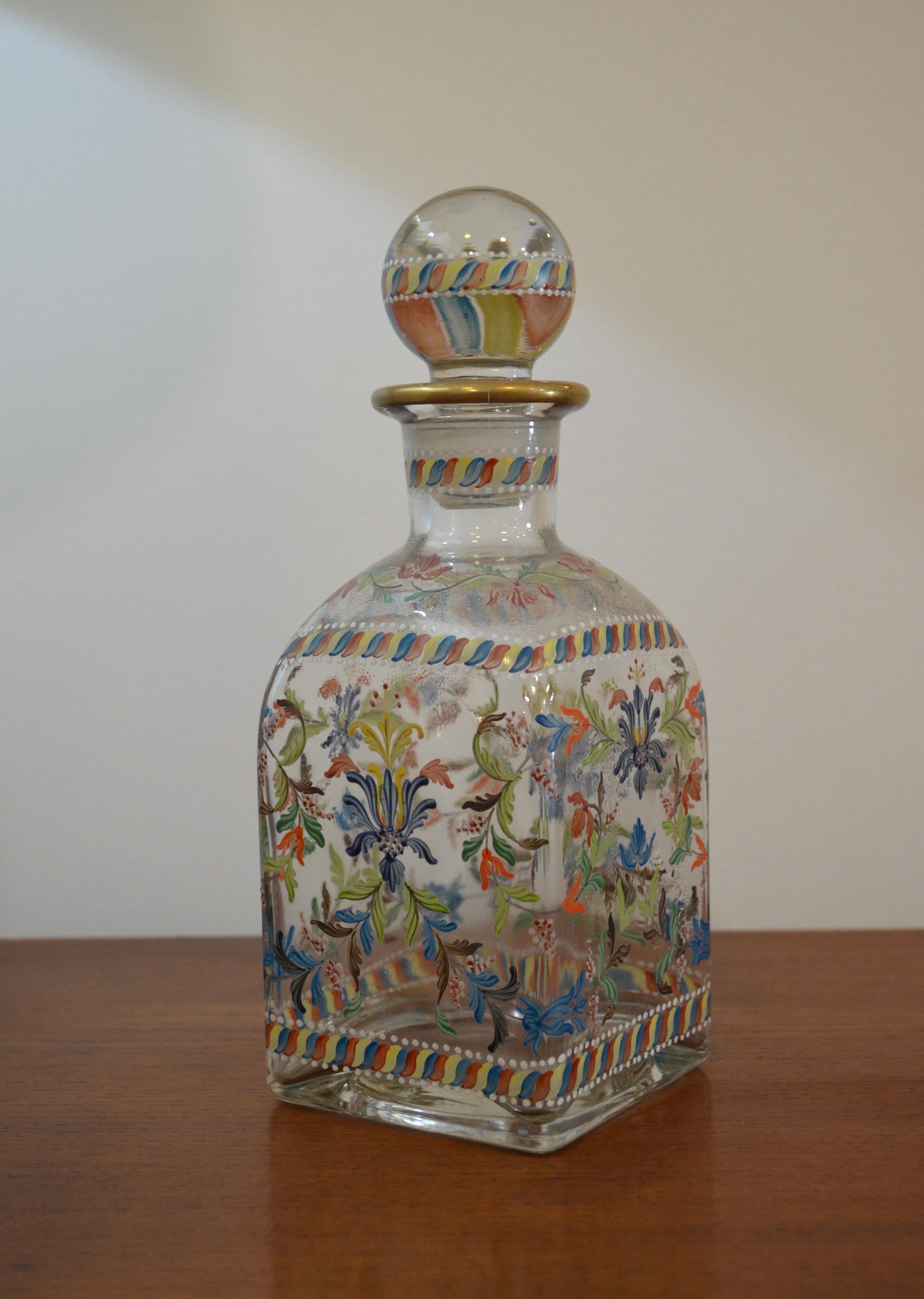 Elegante decantador de cristal soplado a mano, fabricado en Portugal en los años 50-60. Esta hermosa pieza presenta un vibrante diseño floral, delicadamente pintado a mano con esmalte de colores. Su tapón original está adornado con los mismos