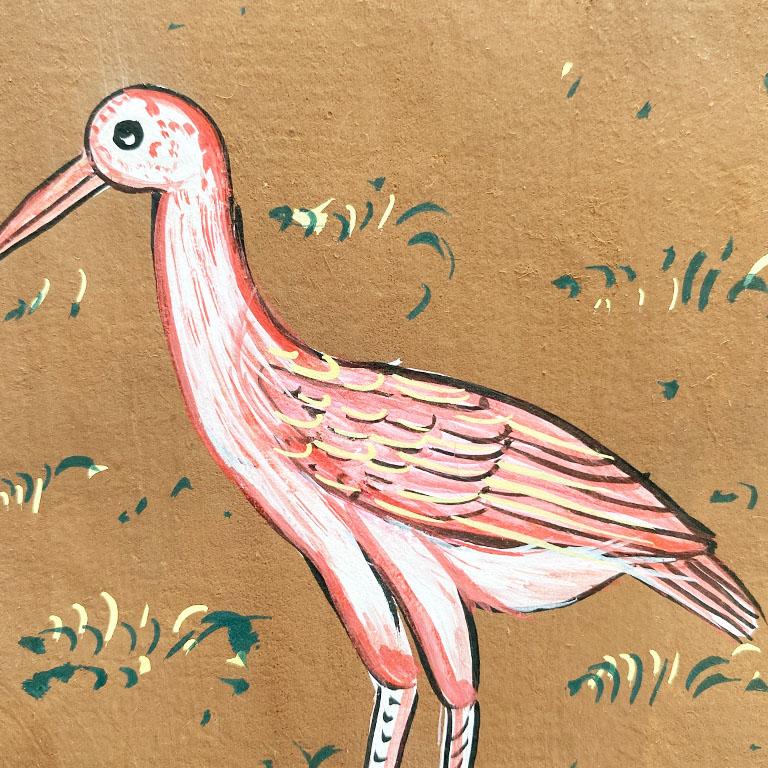 A fabulous piece of Folk Art created in India. This painting depicts a pink bird on a brown background. He stands among a lush green and yellow field of foliage. A yellow border surrounds the piece at the edges. 

We think this would be gorgeous