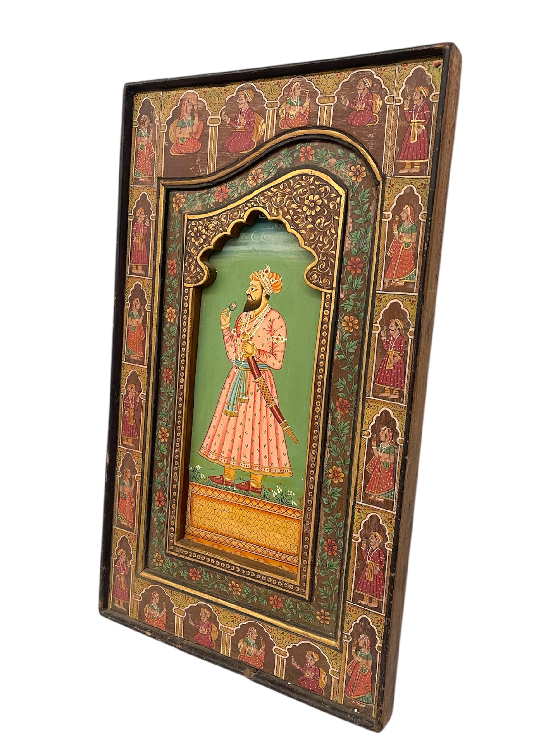 Magnifique panneau de portrait sur bois de style moghol indien, peint à la main, représentant une figure noble au rendu complexe dans un cadre arqué et orné. La figure centrale est représentée en tenue traditionnelle, tenant une fleur et une épée au