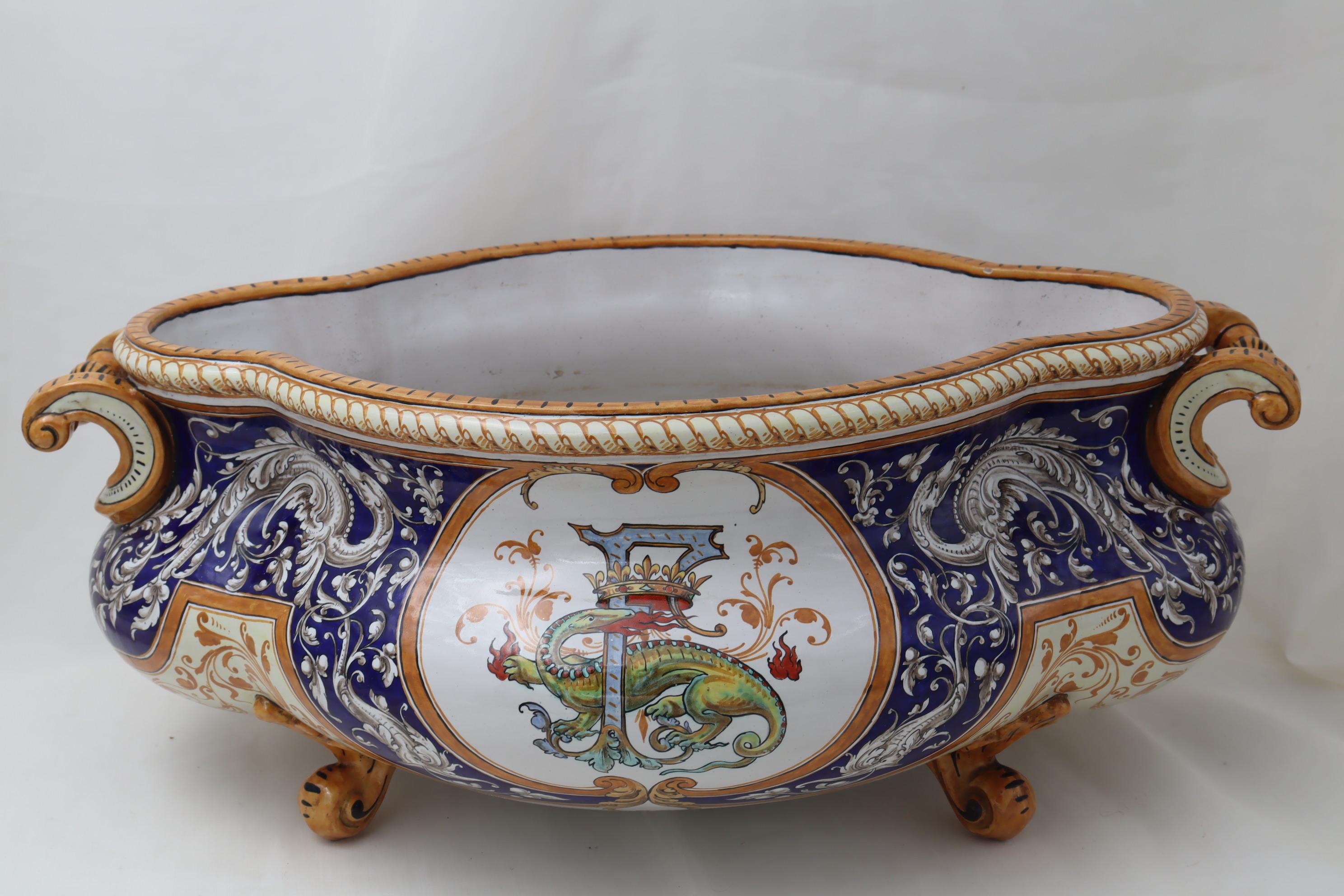 This very large bombe shaped two handled faience jardiniere is by Ulysse Besnard of Blois, France, and rests on four feet. The hand painted decoration includes swirling arabesques and dragons, and on each side in a central cartouche is a hand