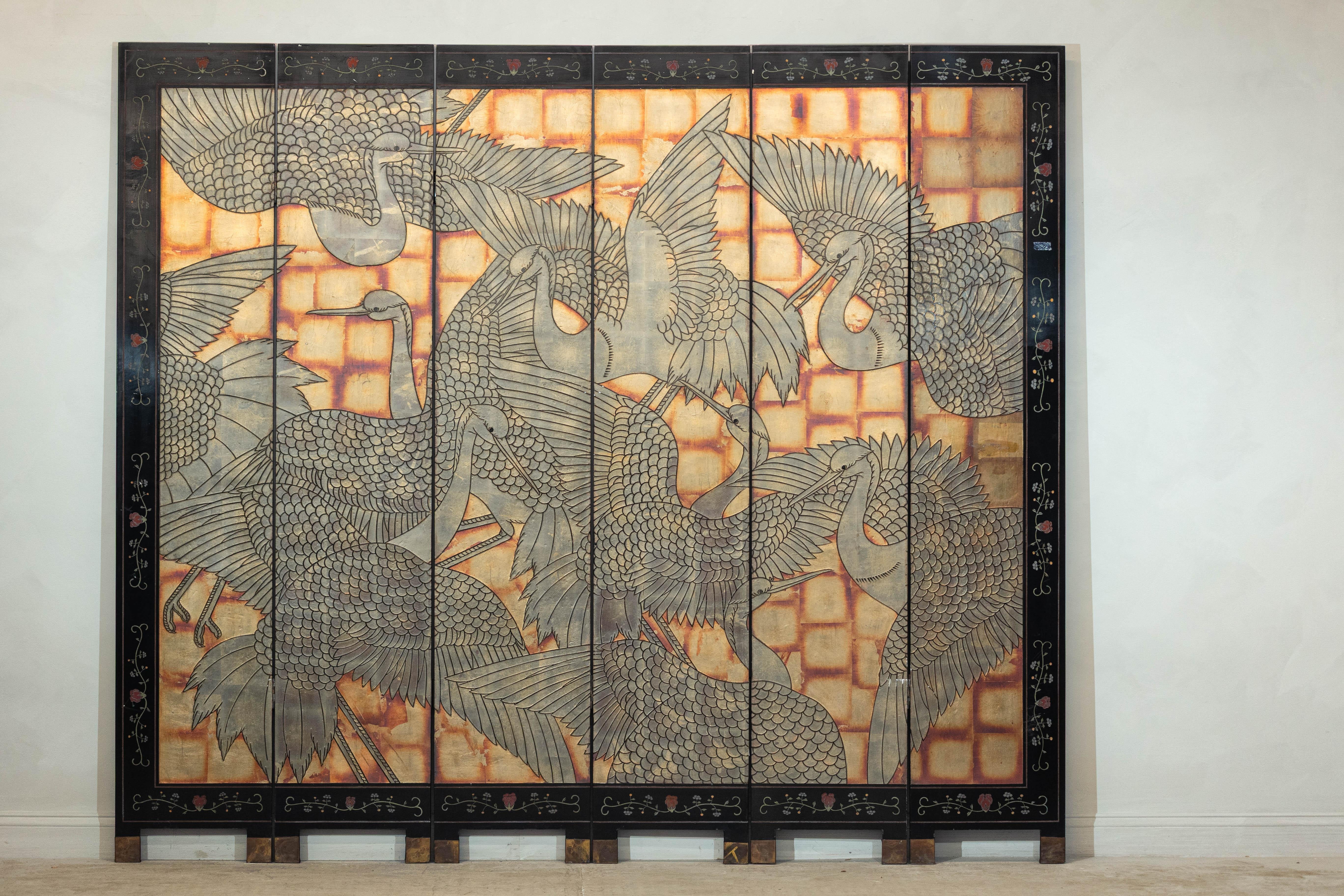 Paravento laccato a sei pannelli con gru rosse in volo. Realizzato in una tavolozza riccamente stratificata di ocra caldo, nero e morbidi toni metallici, questo paravento vintage a sei pannelli presenta un suggestivo tableau di gru dal ciuffo rosso