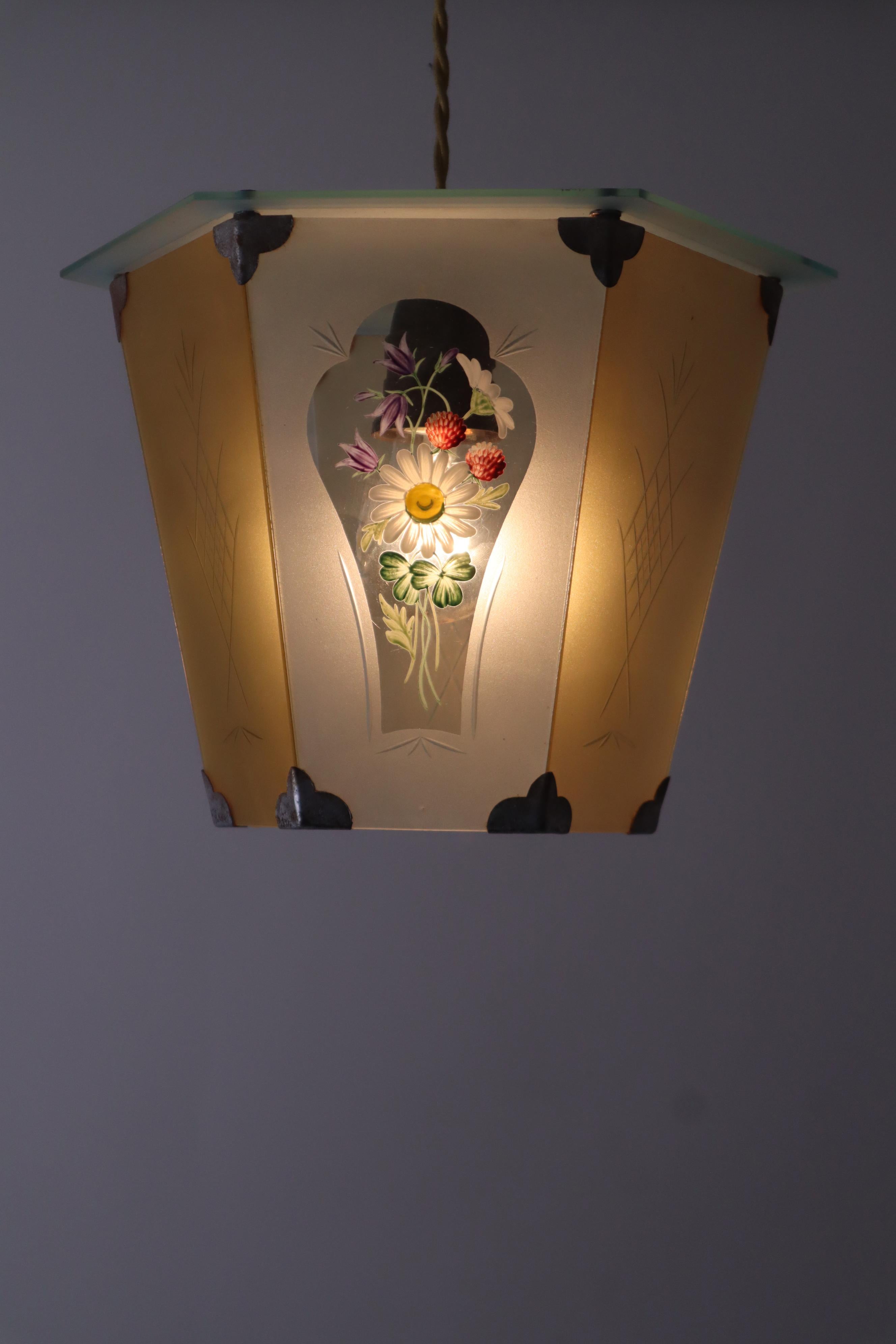 Déjate hechizar por esta encantadora lámpara linterna de principios del siglo pasado. Mira las magnolias, campanillas, flores de trébol y tréboles pintados a mano que decoran bellamente el vaso. Fíjate en los laterales de la linterna grabados a mano