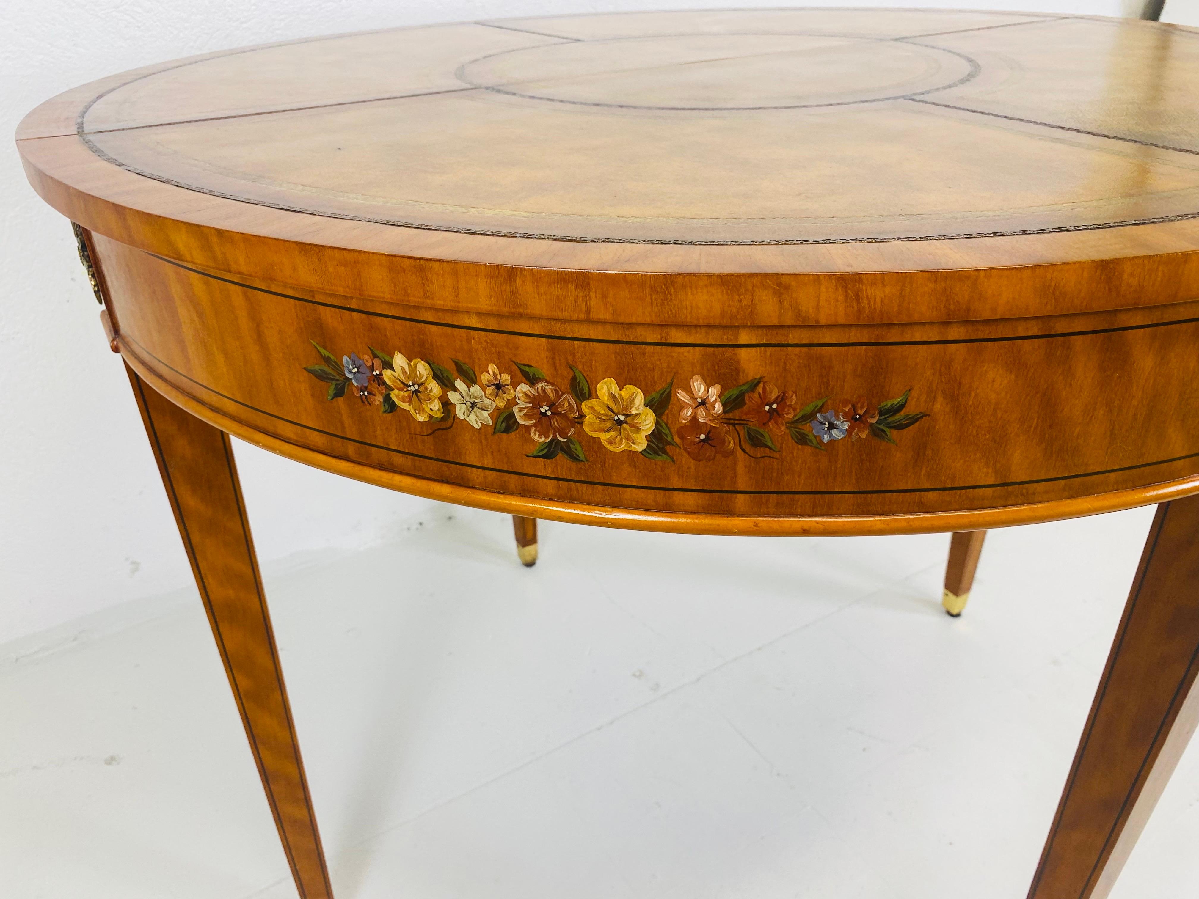 Il s'agit d'une élégante table d'appoint/table de jeu en cuir peint à la main. Cette table présente une décoration florale peinte à la main sur le plateau, le tablier et les pieds. Le plateau de la table est recouvert d'un magnifique cuir fauve dont