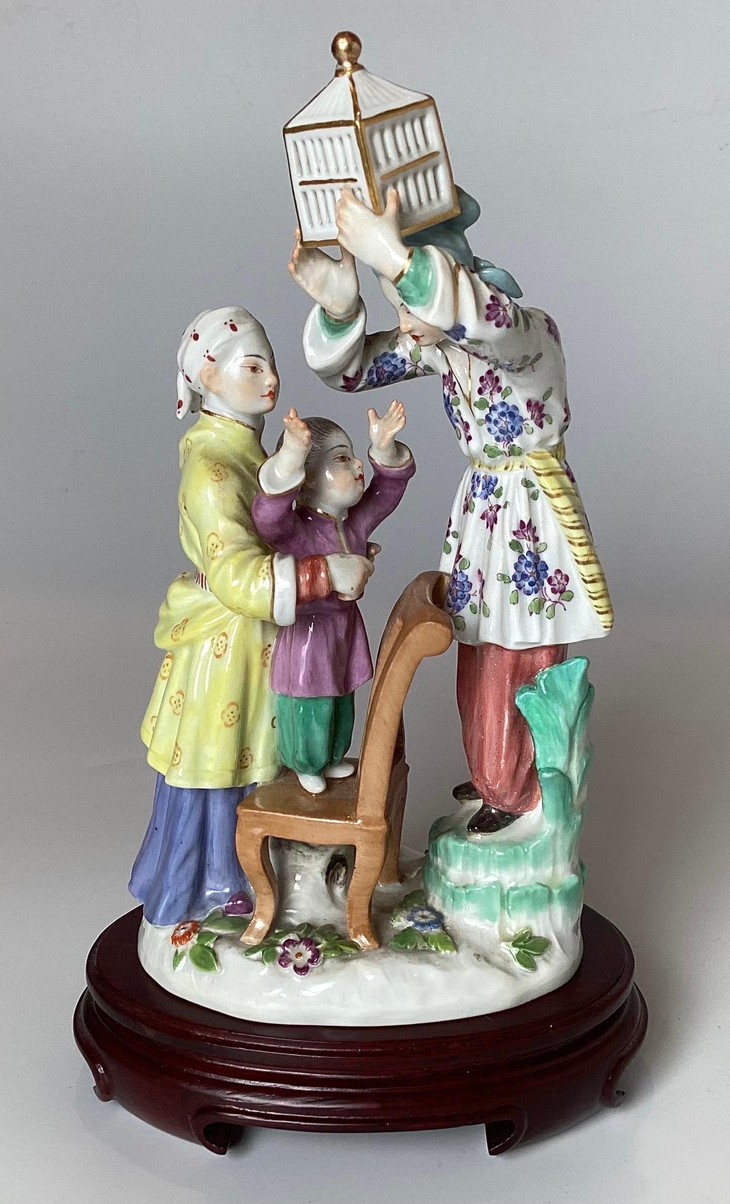 Meissen porcelain figure chinoiserie style on wood base.  The hand painted figures one holding a bird cage with the Meissen blue under glaze mark.  The wood stand added later is included. 