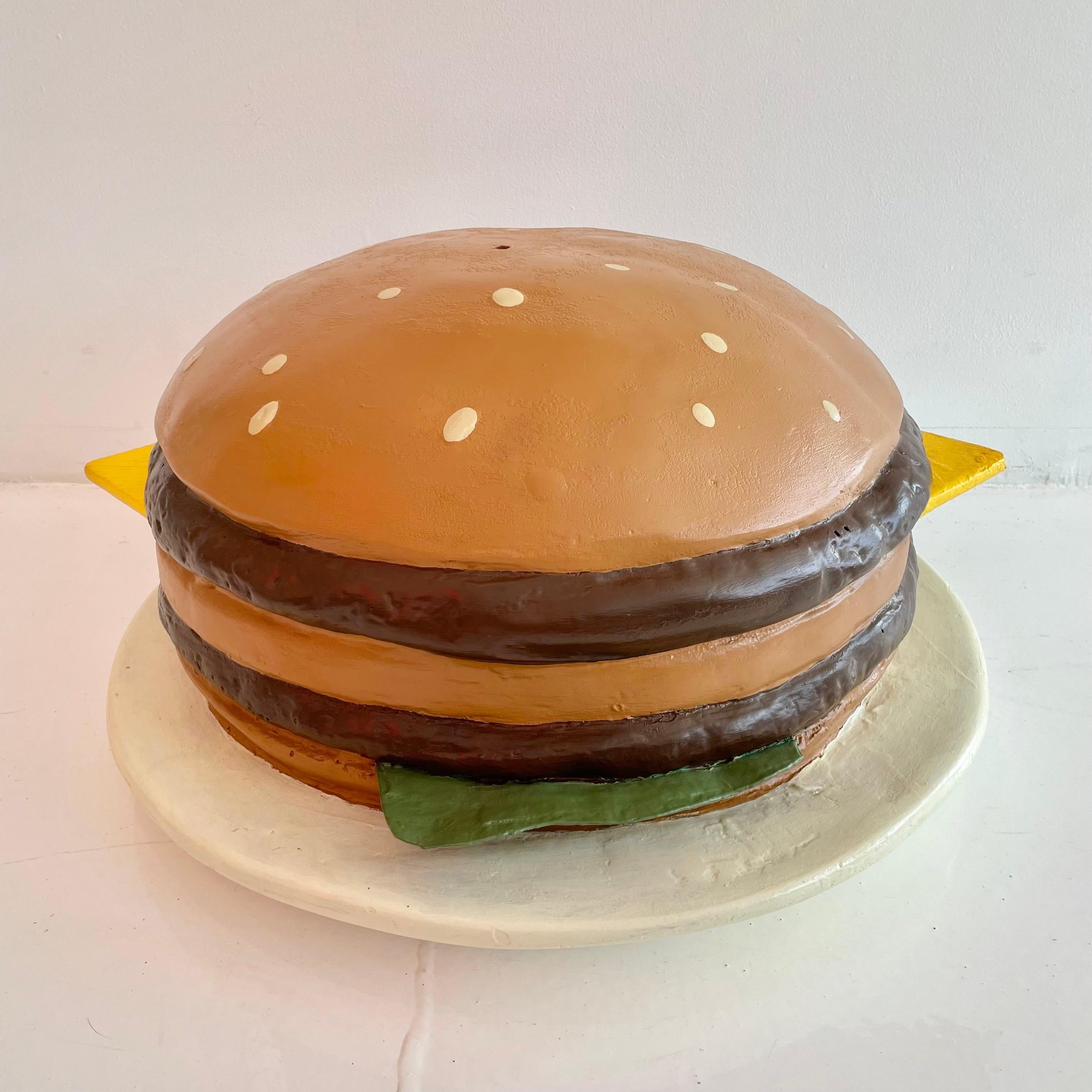 Oversized vintage cheeseburger pop art in fiberglass. Likely used as a store display. Hand made in fiberglass and hand painted with great detail. Triple layer bun, two hamburger patties, cheese and lettuce sitting atop a white plate. Bright and eye