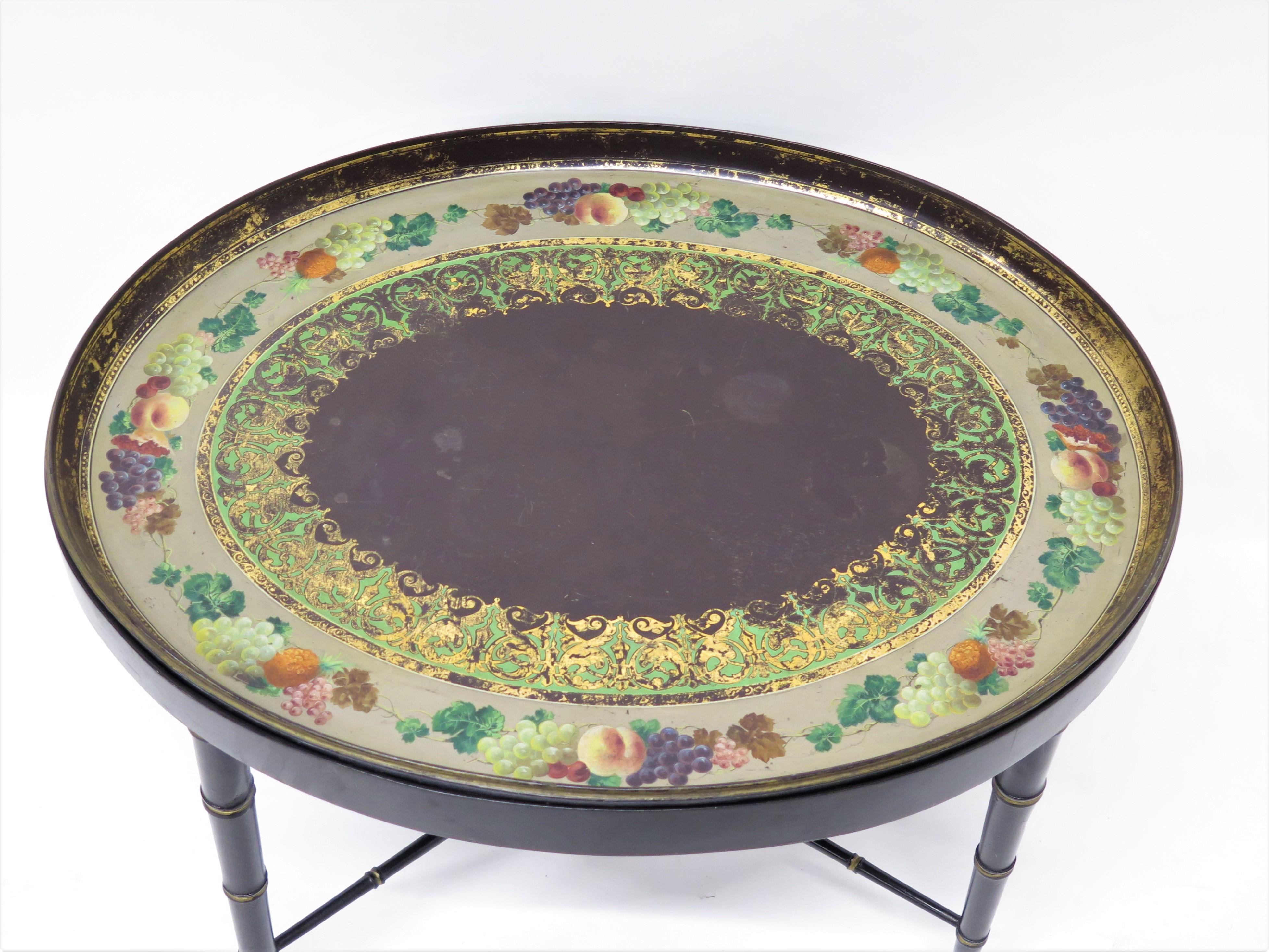 a large oval paint and parcel gilt papier-mâché tray on a faux bamboo stand with X-stretcher, some losses to gold embellishments on green and gold inner border, beautiful hand-painted fruit, including grapes and grape leaves border, England, 19th