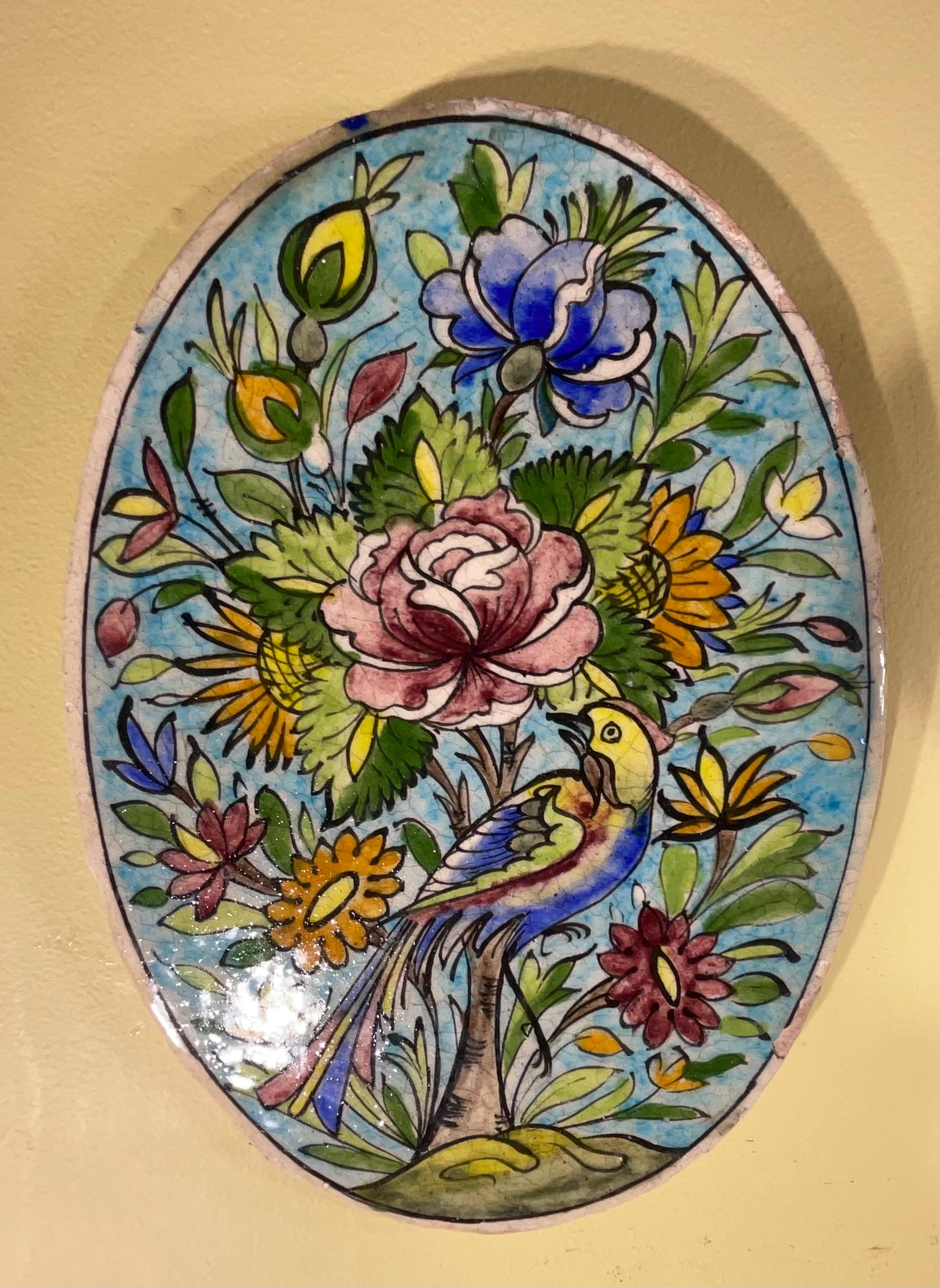 Entrez dans le monde captivant de l'art persan avec ce magnifique carreau de céramique peint à la main. Ce carreau ovale unique présente un design vibrant et méticuleusement détaillé, mettant en scène une riche tapisserie de fleurs épanouies et un