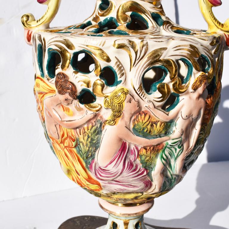Italian porcelain hand painted traditional urn shape lamp by Capo Di Monte. Urn shape in form, the top is accented with two handles with swirls highly decorated in light pink, gold and yellow. The lamp widens at the bottom of the handles and tapers