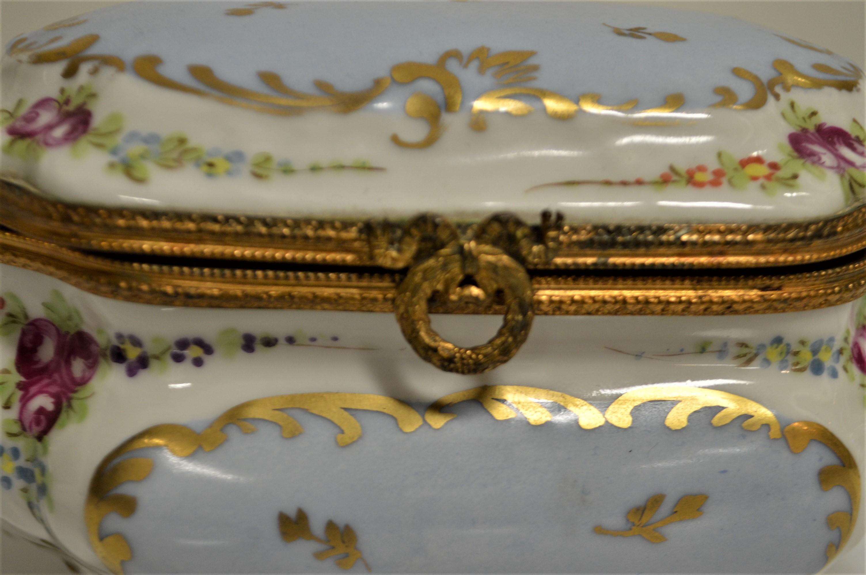 This precious hand painted porcelain jewelry box was made in France for Saks NY 5th Anniversary, 1907.
The interior is very clean, shows hand painted pink flowers. The bronze decorative rim is finished with an attractive wreath and bow clap that