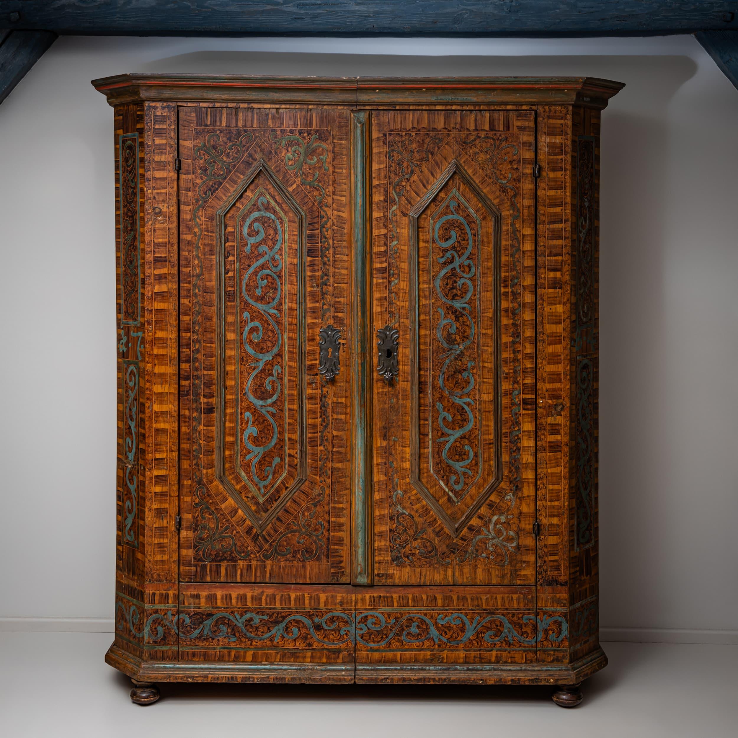 Armoire country a due ante realizzato in legno di conifera, con angoli smussati e cornice piatta e modanata. Le porte sono decorate con pannelli esagonali. La verniciatura originale di colore marrone imita il parquet ed è completata da delicati