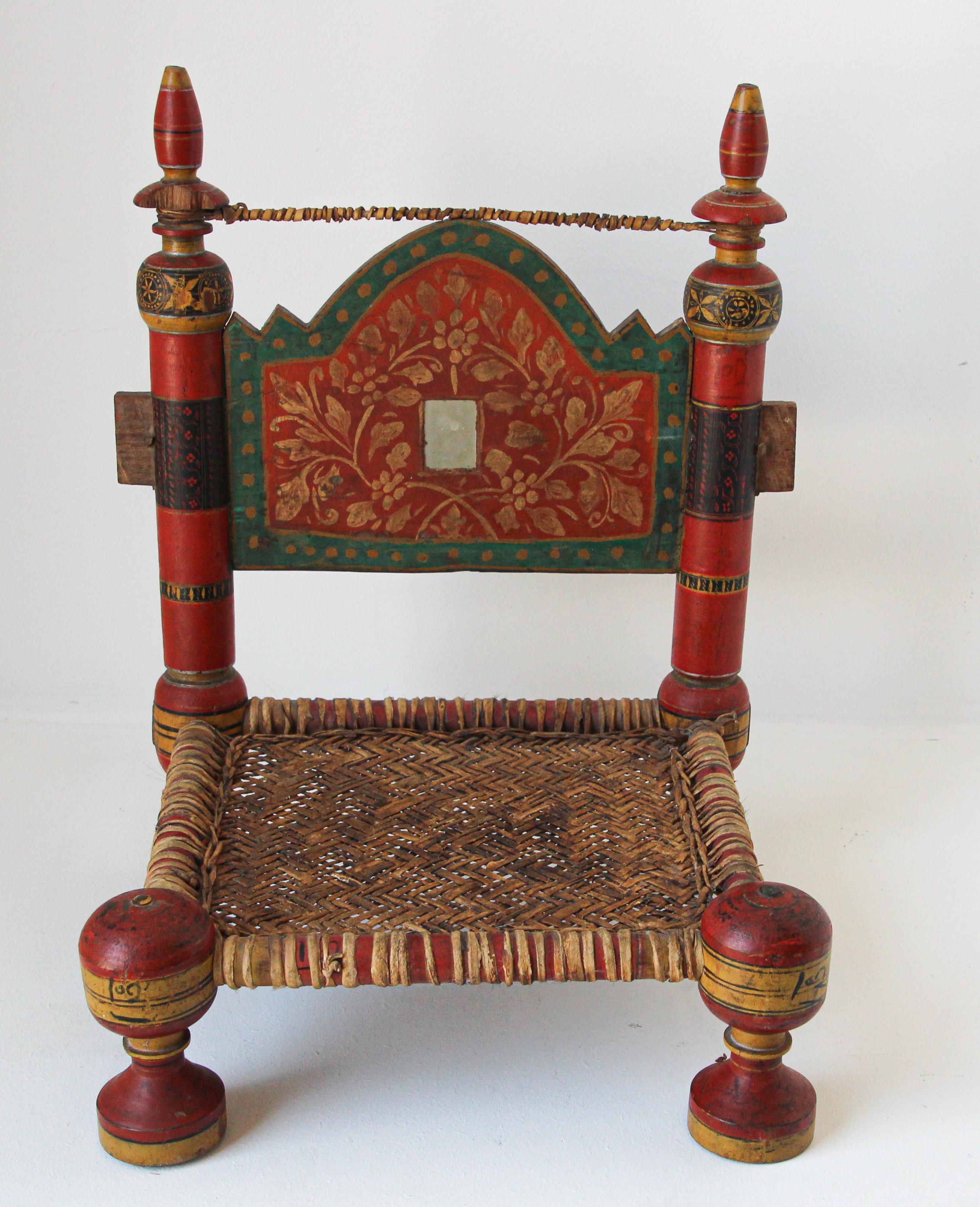 Indian Rajasthani low chair with red, green, black and gold, with caned handwoven leather seat.
An antique Indian rustic low wooden chair from the 19th century. 
Charming our eyes with its rustic appearance, this low wooden chair features a straight