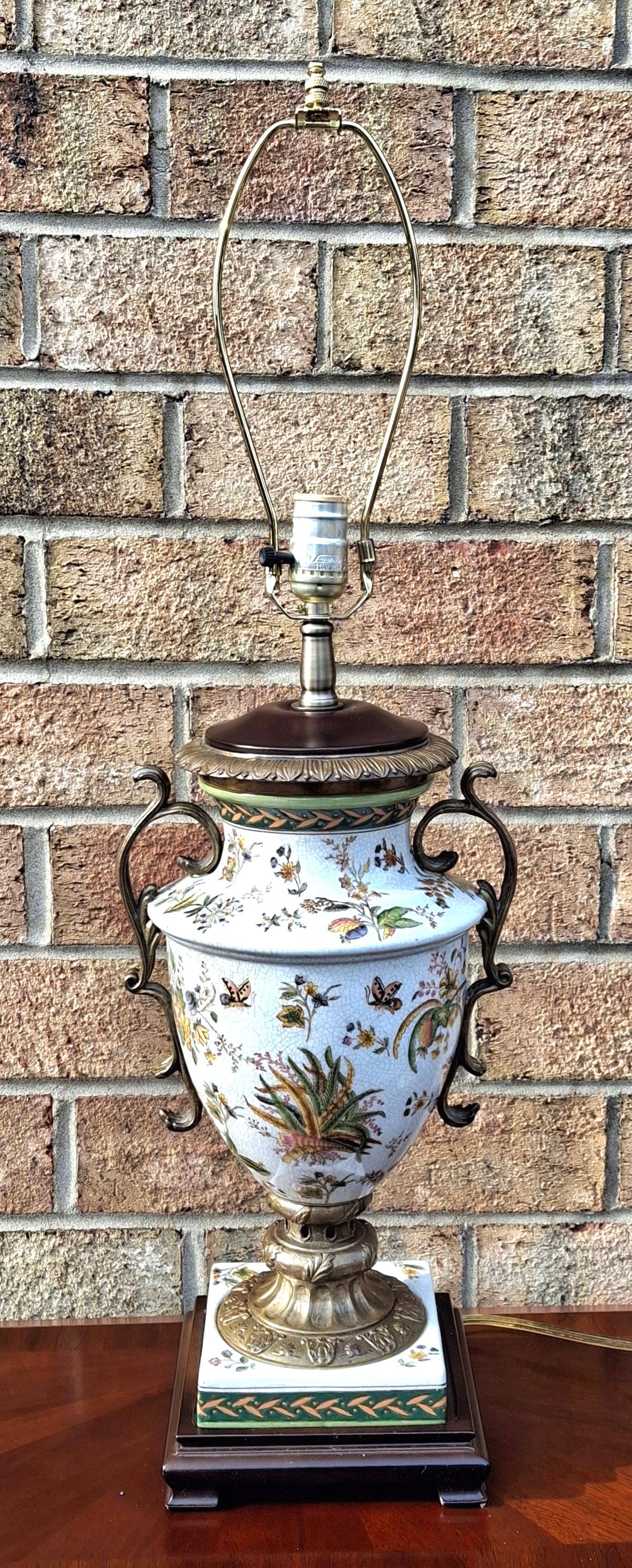 Lámpara de sobremesa Urna de porcelana vintage con acabado craquelado, pintada a mano con motivos florales y mariposas, montada sobre una base de latón y madera. 
La base de la lámpara tiene forma de urna de porcelana, con intrincados y coloridos