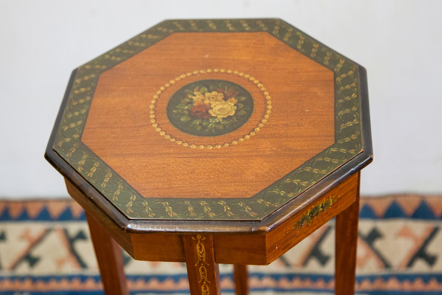 Hand painted satinwood stand, the octagonal top edge painted with an interlaced floral trailing vine. The center of the top has a floral center surrounded by a beadwork border. Tapered legs have painted bellflower with a nicely shaped floral painted