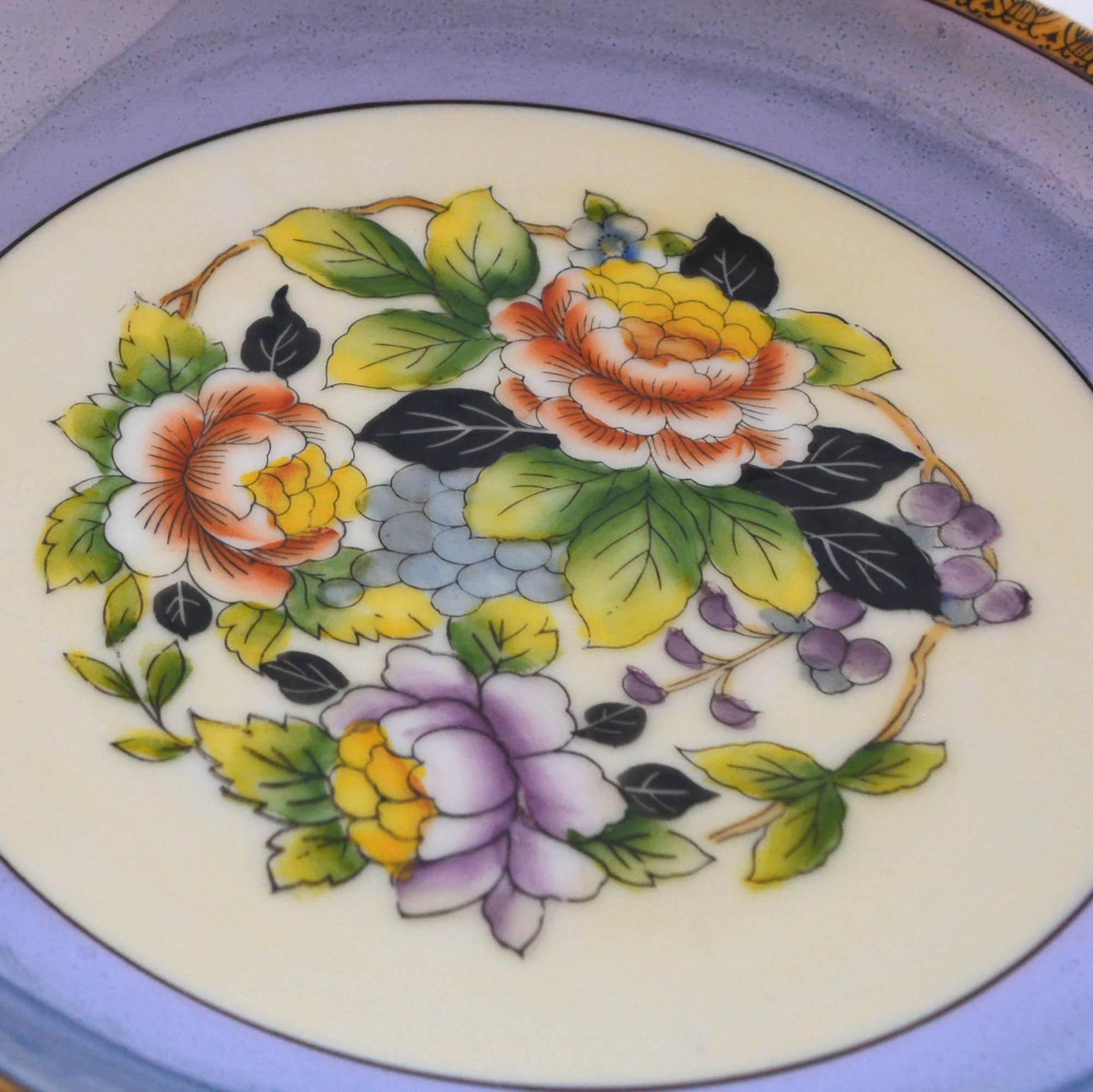 Detailed hand painted cornflower blue Noritake bowl has a shallow bowl and colorful center design. The floral design has burnt red, yellow and purple flowers. The rim is decorated, and the maker's mark in on the bottom.