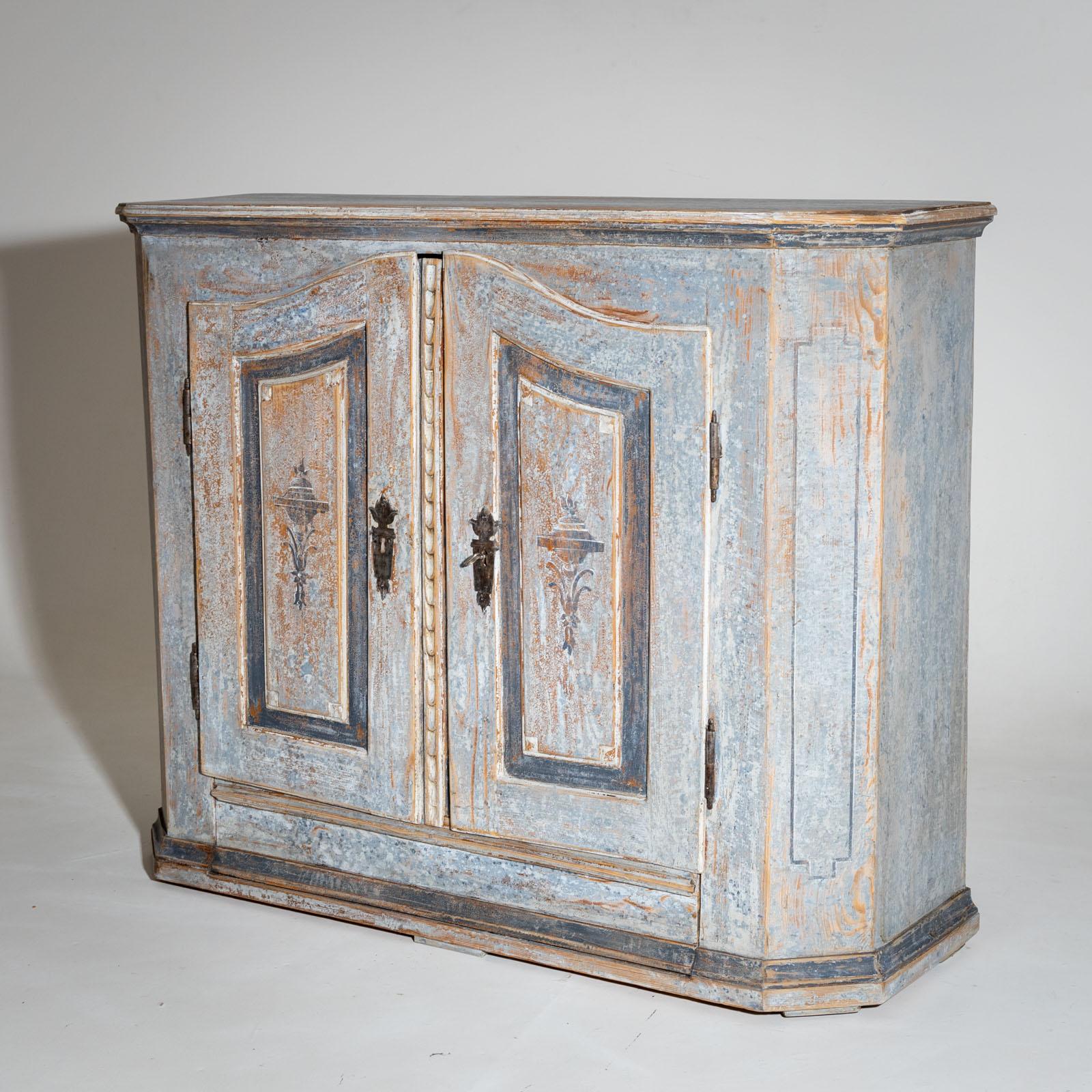 Hand-painted two-door sideboard with beveled corners and curved doors. The panels on the front are decorated with amphorae and set off in dark blue. The body is newly painted and was designed according to historical models and given an antique