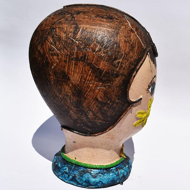 Hand painted head of a woman with short hair. Created from Styrofoam, papier-mâché and rope, this lovely woman is hand painted with short brown hair, blue-green eyes, a blue-collar, and yellow floral designs to her cheeks. She reminds us of a 1970s