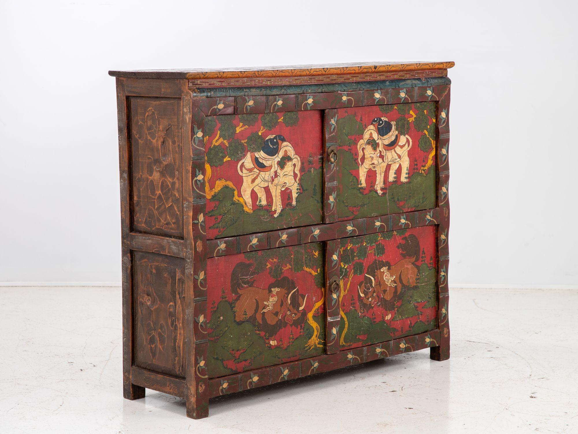 A Tibetan cabinet is a unique and beautifully crafted piece of furniture that is steeped in history and cultural significance. This particular cabinet boasts hand-painted details on each of its doors, with elephants on the upper doors and bulls on