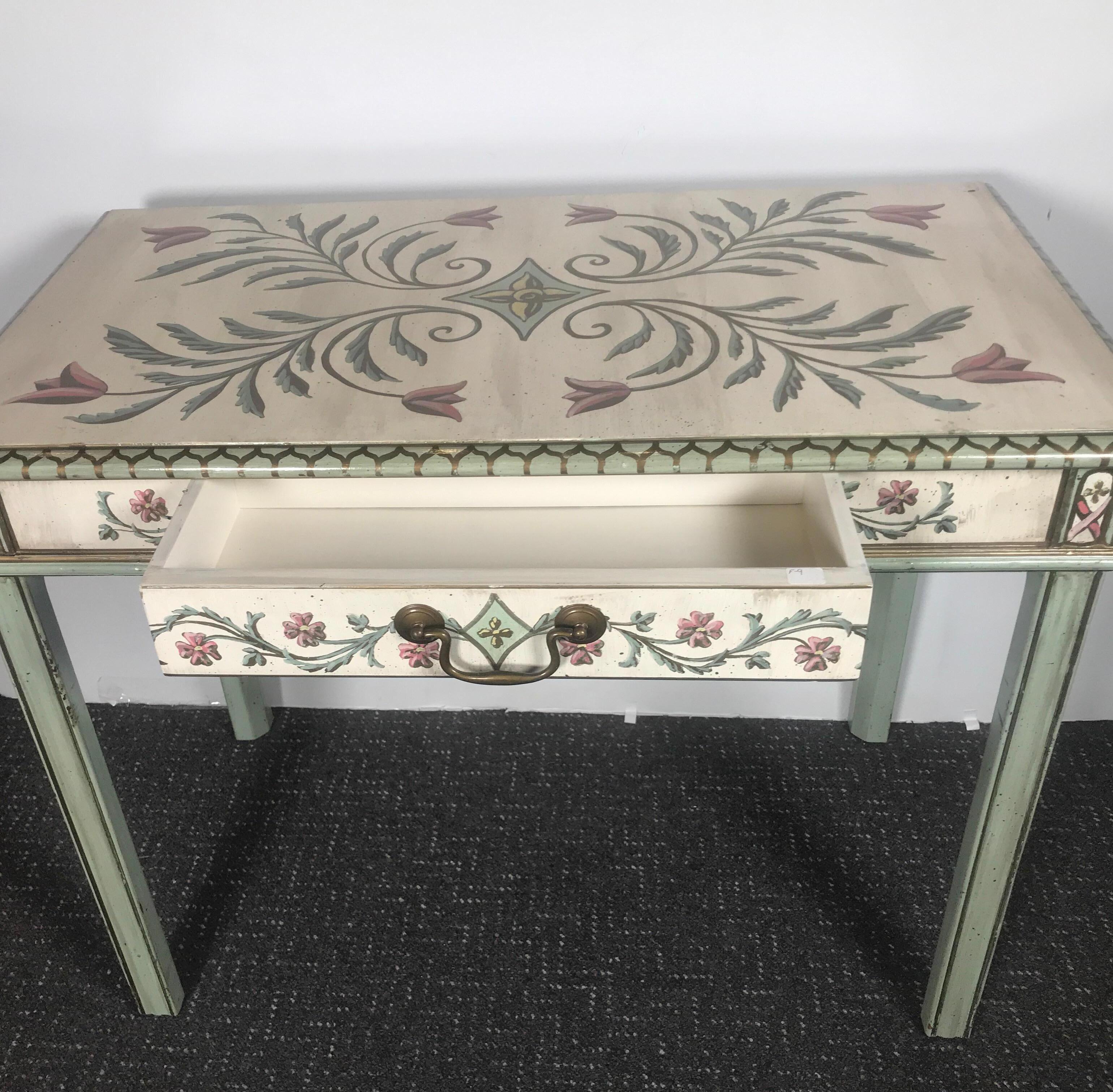 A beautifully hand painted table vanity desk with off-white background with scrolling and floral details. The simple form with one drawer.