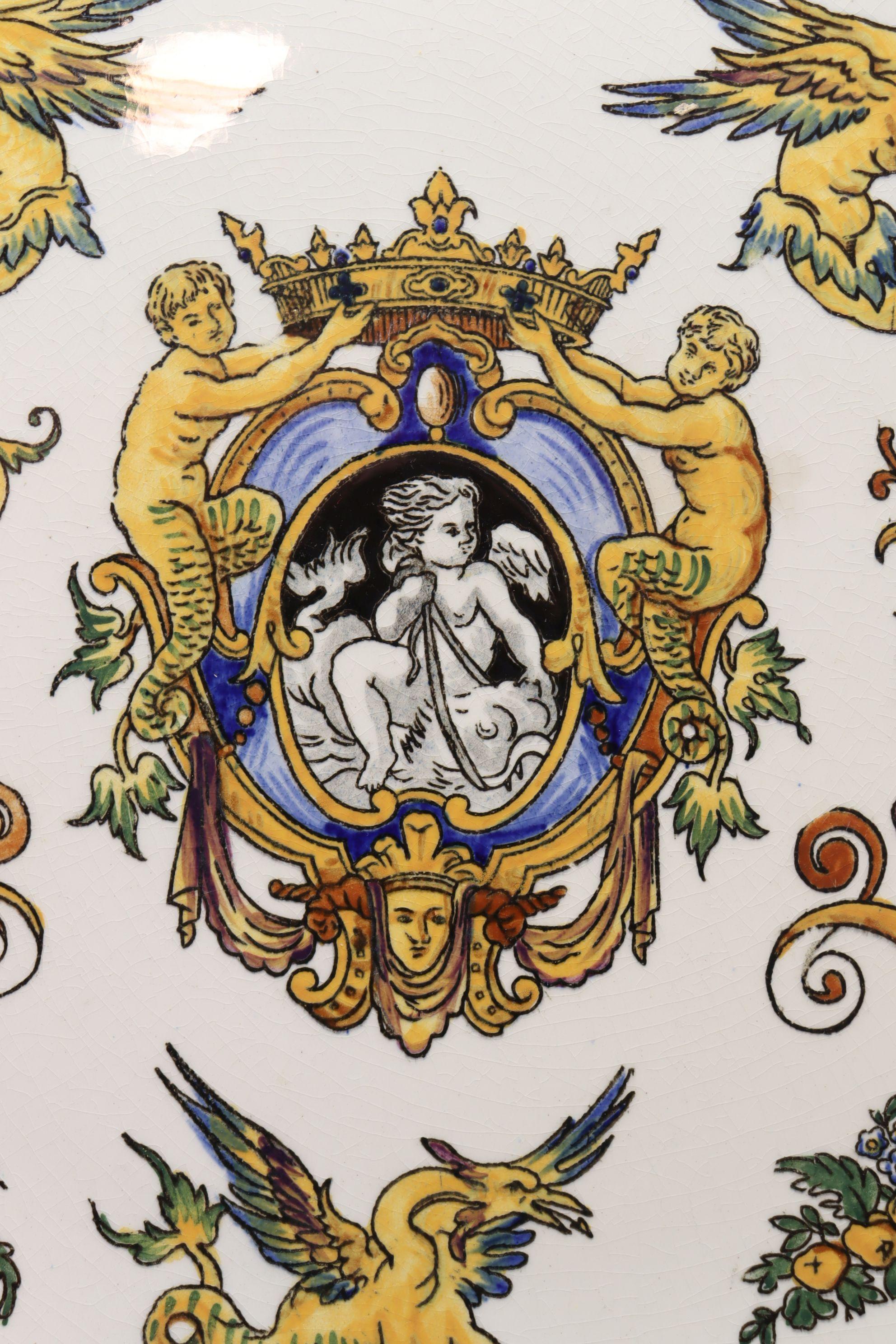 Diese sehr farbenfrohe, handbemalte Wandtafel aus Keramik von Gien aus Frankreich ist mit einem zentralen, gefälschten Wappen verziert, das von Fabelwesen flankiert wird, über denen sich ein Wassermann und eine Meerjungfrau befinden. Der äußere Rand
