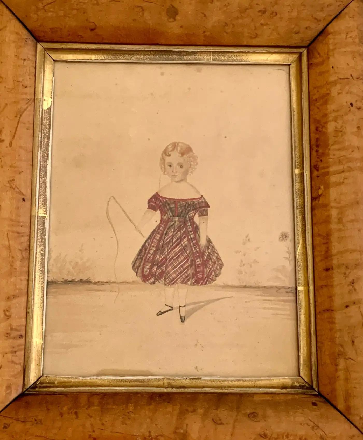 A small, mid-19th-century English School watercolor portrait of a young girl with her hair in perfect curls and wearing a plaid dress. 
She has a serious look appropriate for standing still while this important portrait is painted.
Her expression of
