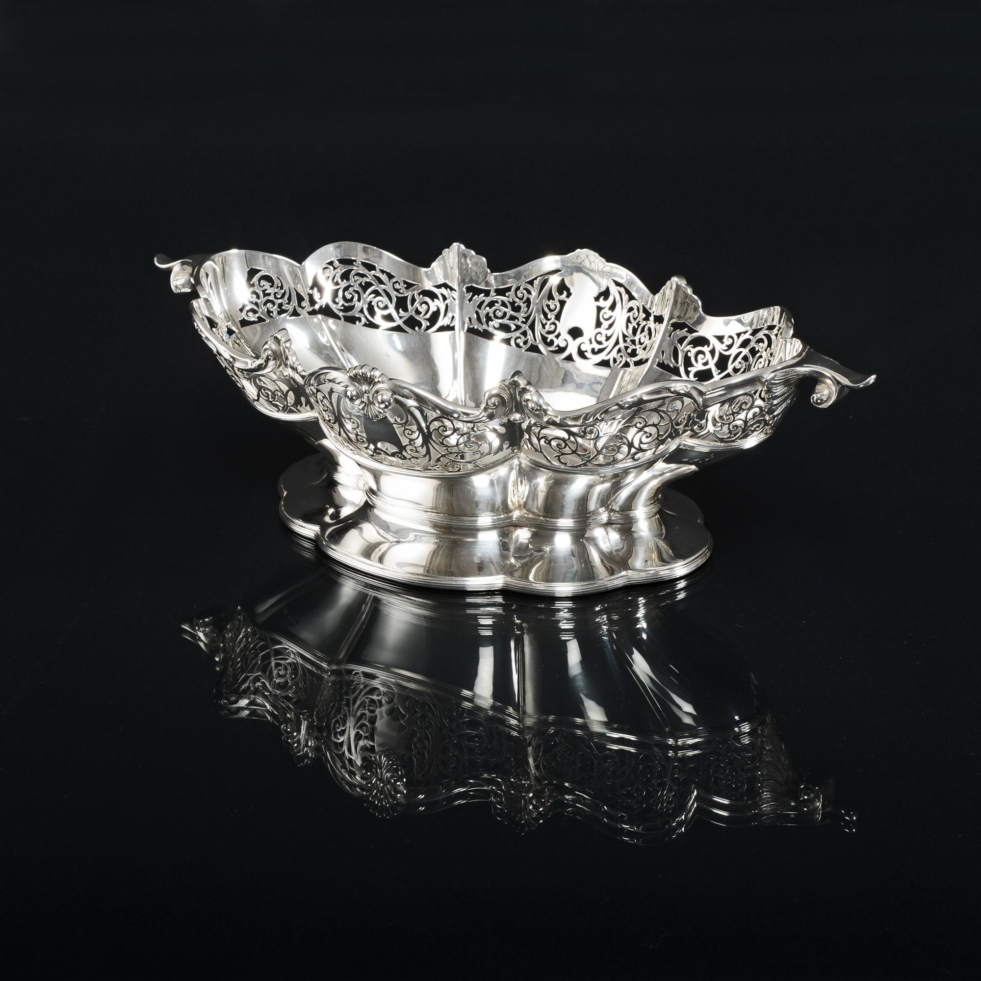 A charming silver oval and shaped bowl featuring a crisply hand-pierced gallery around the upper half of the body and a cast and applied leaf and fanned flute rim. Two graceful curled scroll handles sit at either end and three bands of applied