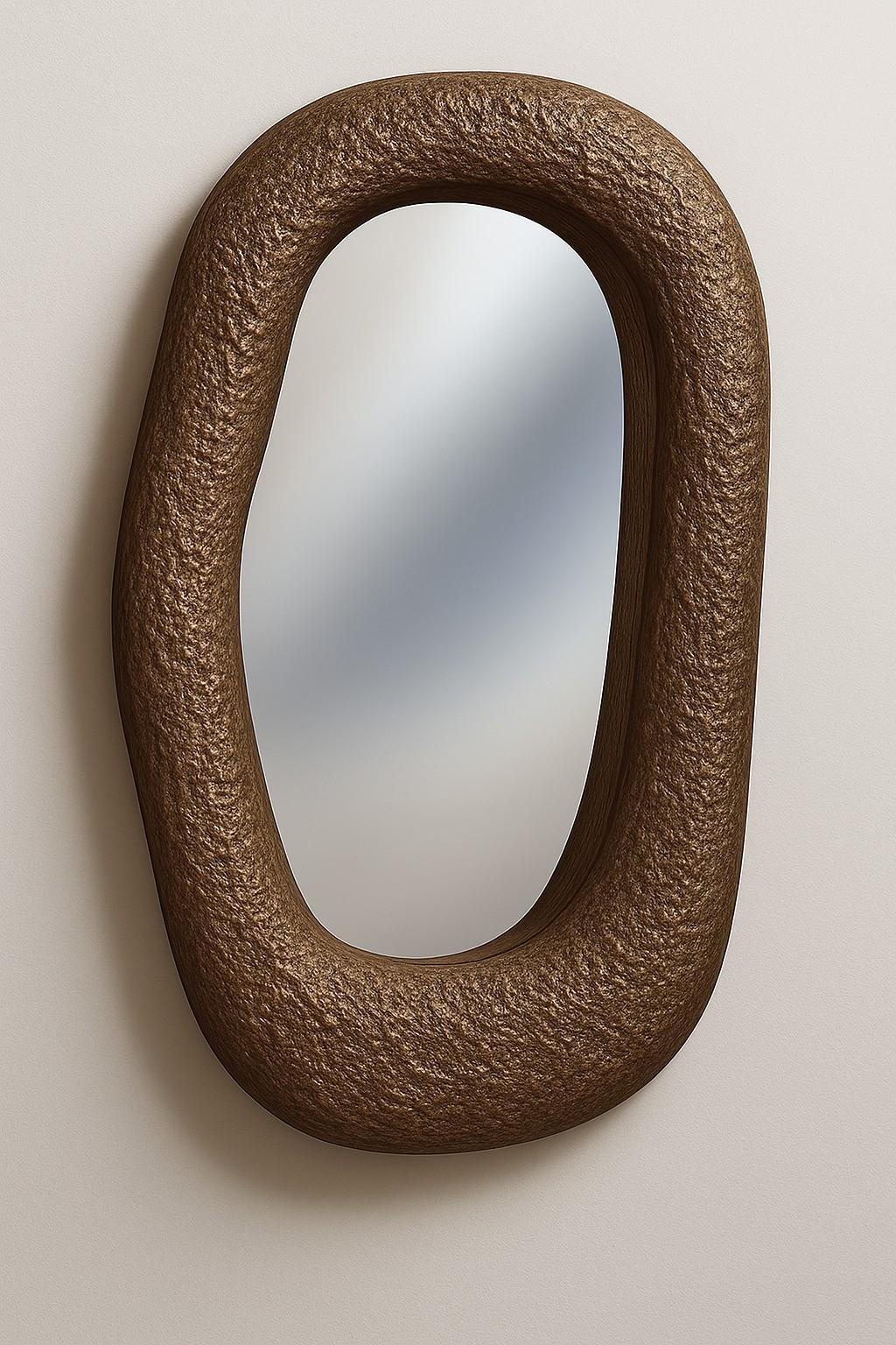 Scultoreo e organico, questo specchio presenta una spessa cornice a forma di ciottolo con una ricca finitura in bronzo opaco che evoca la profondità tattile del metallo martellato. La sua silhouette ovale irregolare e allungata ricorda i contorni