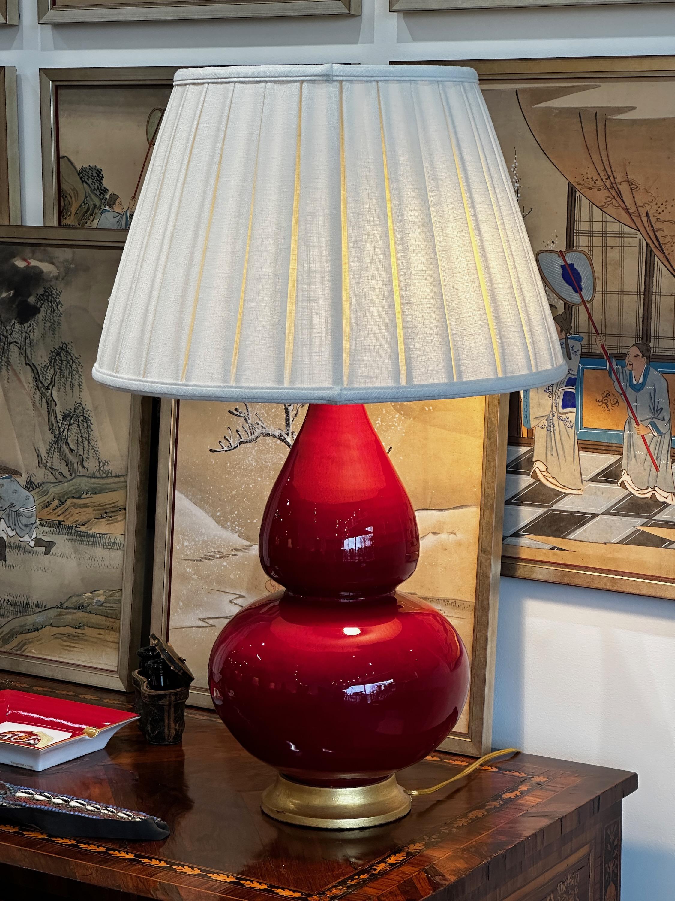 An iconic ceramic double gourd lamp with a deep scarlet glaze on a giltwood base.