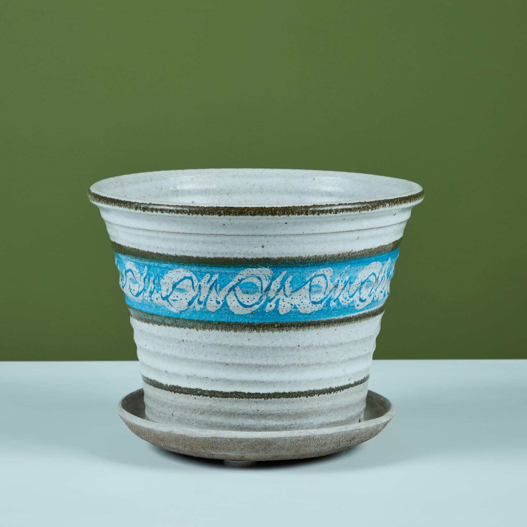 Hand thrown stoneware table planter with water catch. The planter features a glazed exterior in cream and blue tones that tapers towards the bottom with an attached glazed water catch dish. There are two holes for release of water into the