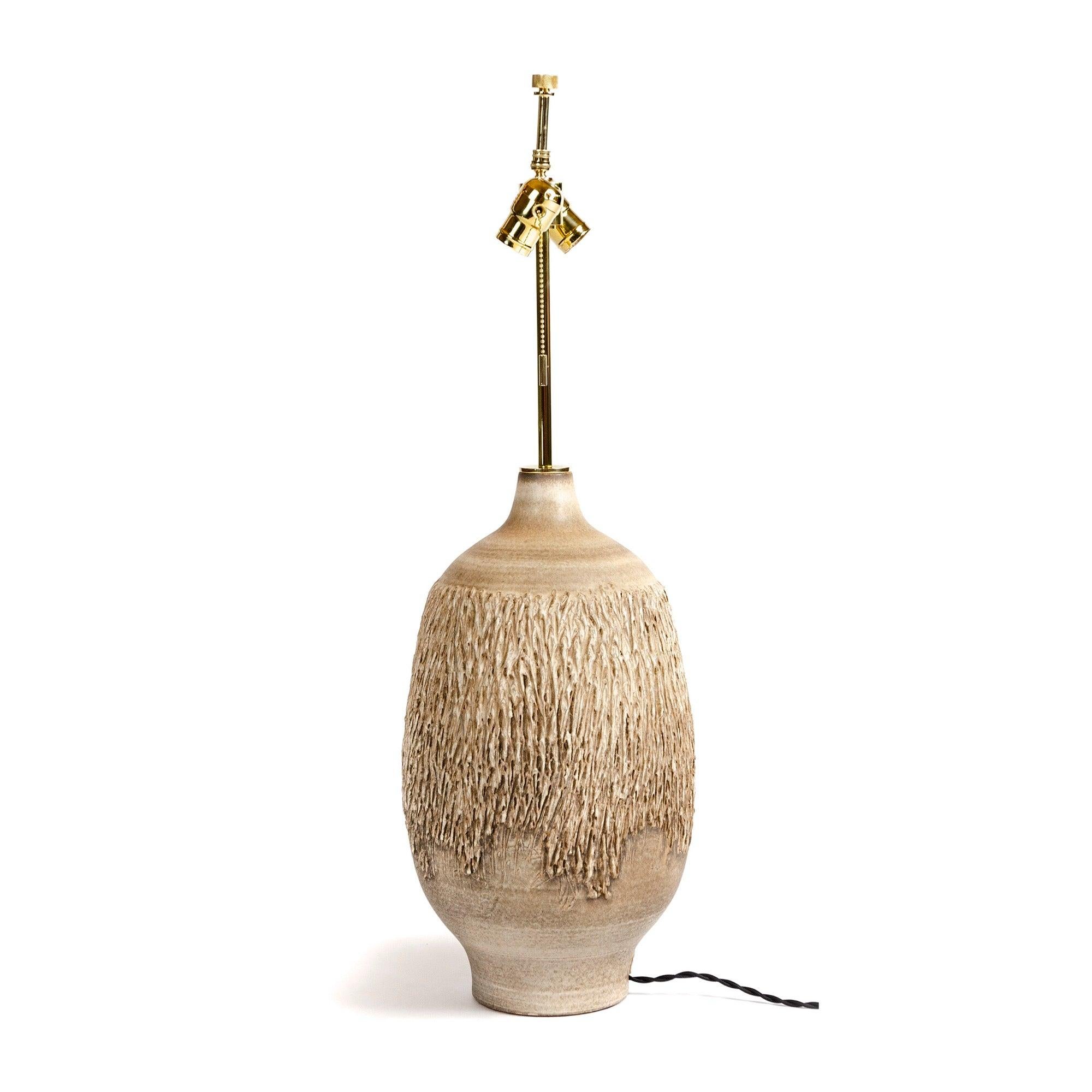 Une belle lampe de table jetée à la main. Glacé dans des tons sableux avec des détails verticaux texturés appliqués à la main, ressemblant à l'écorce d'un arbre. Le câblage a été refait à neuf avec des accessoires électriques en laiton massif dans