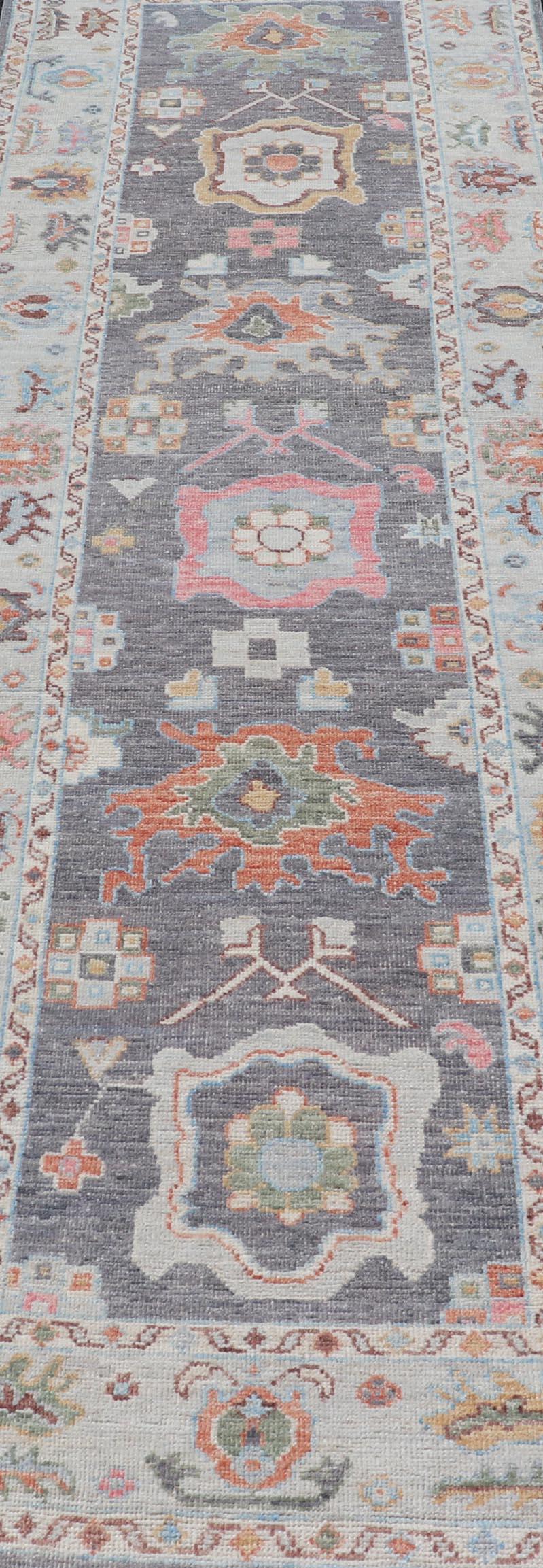 
This Afghan Oushak runner features a grand motif, showcasing from the border to the field with a vibrant elegance that pops against the light blue-gray border, as well as the charcoal background throughout the center. The intricate details in the