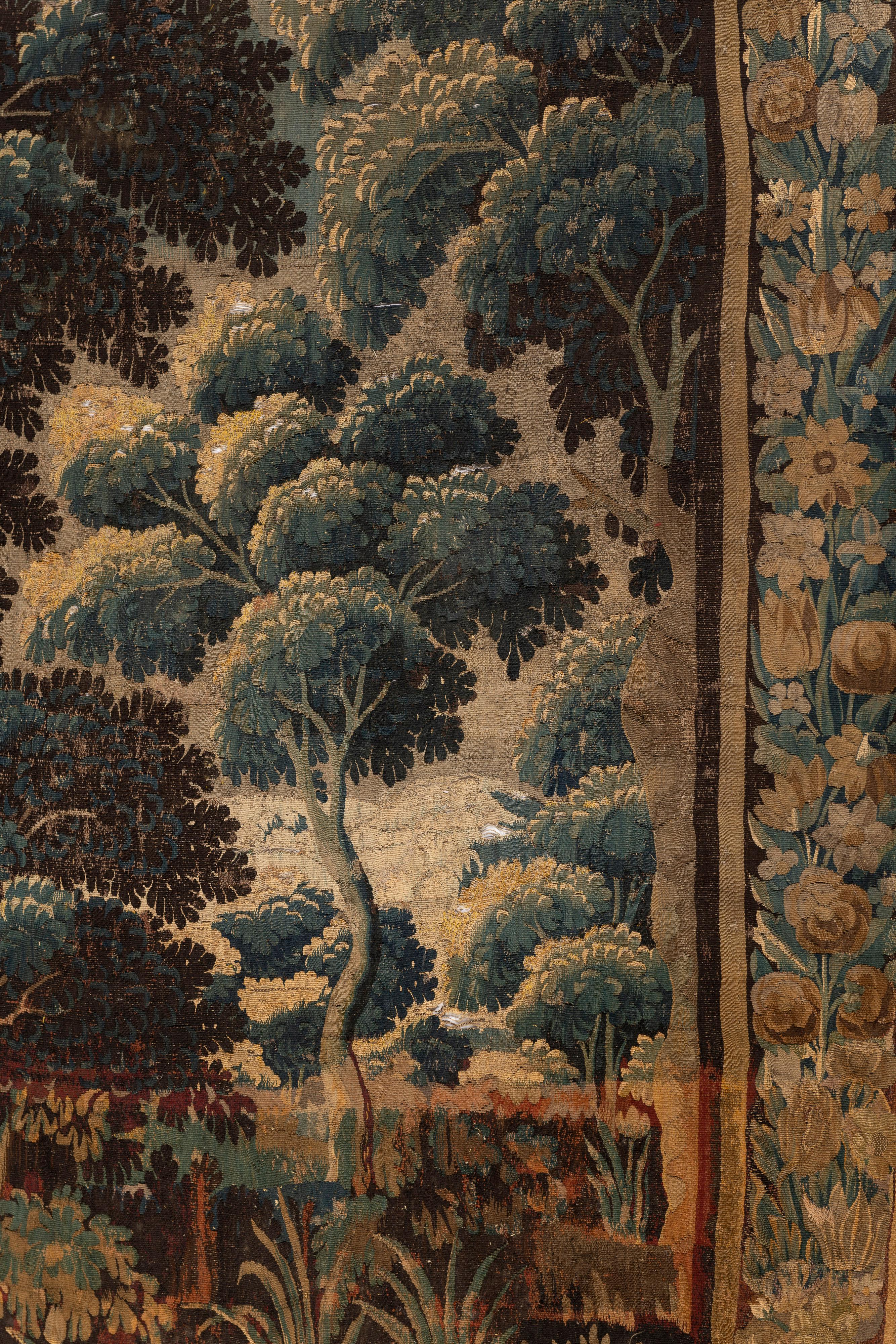 Large Classical French Tapestry, hand-woven of a blend of silk, wool and linen, features a serene landscape with a lovely floral border. The flowers, trees and sky are created in lush, muted hues of blue, green, brown and gold. Enhance your space by