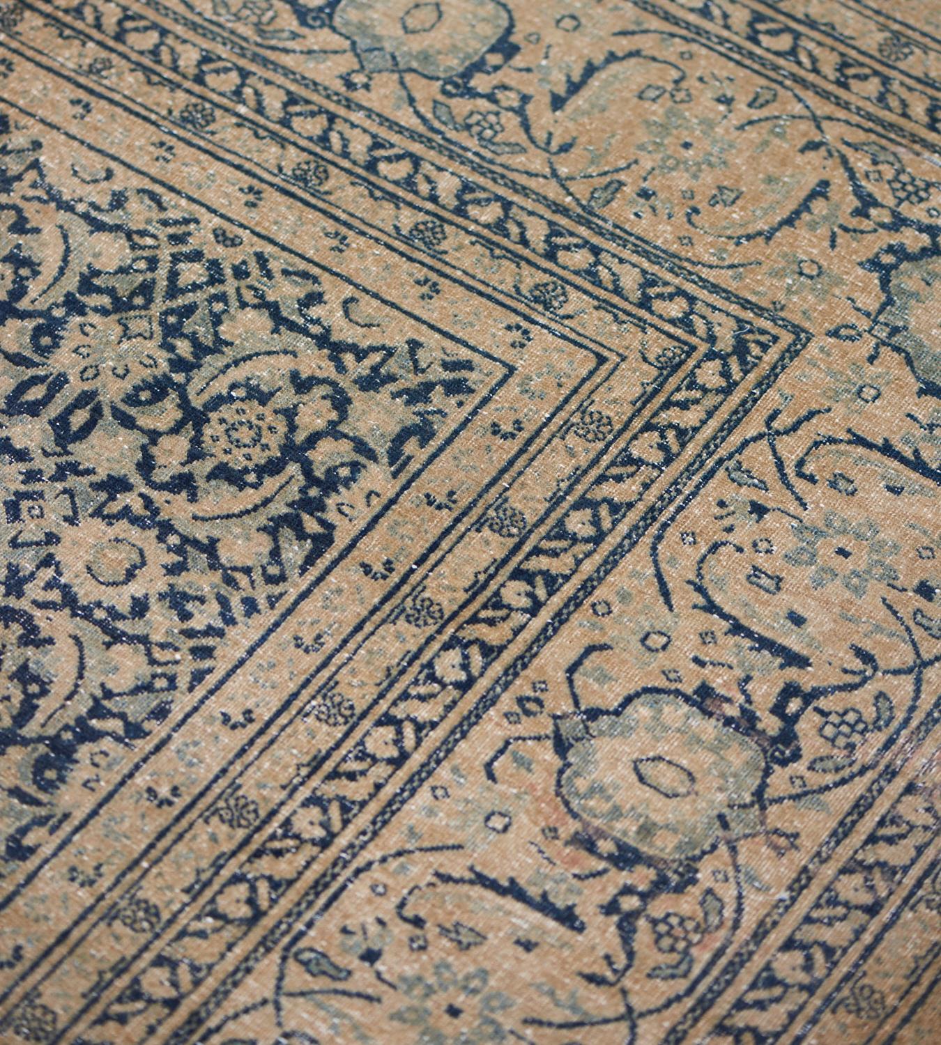 Cet ancien tapis persan Tabriz, datant de 1900, présente un champ bleu royal nuancé avec un motif herati brun chamois, dans une bordure de tortue-palmette et de vigne florale serpentant entre des bandes triples de vigne florale brun chamois et bleu
