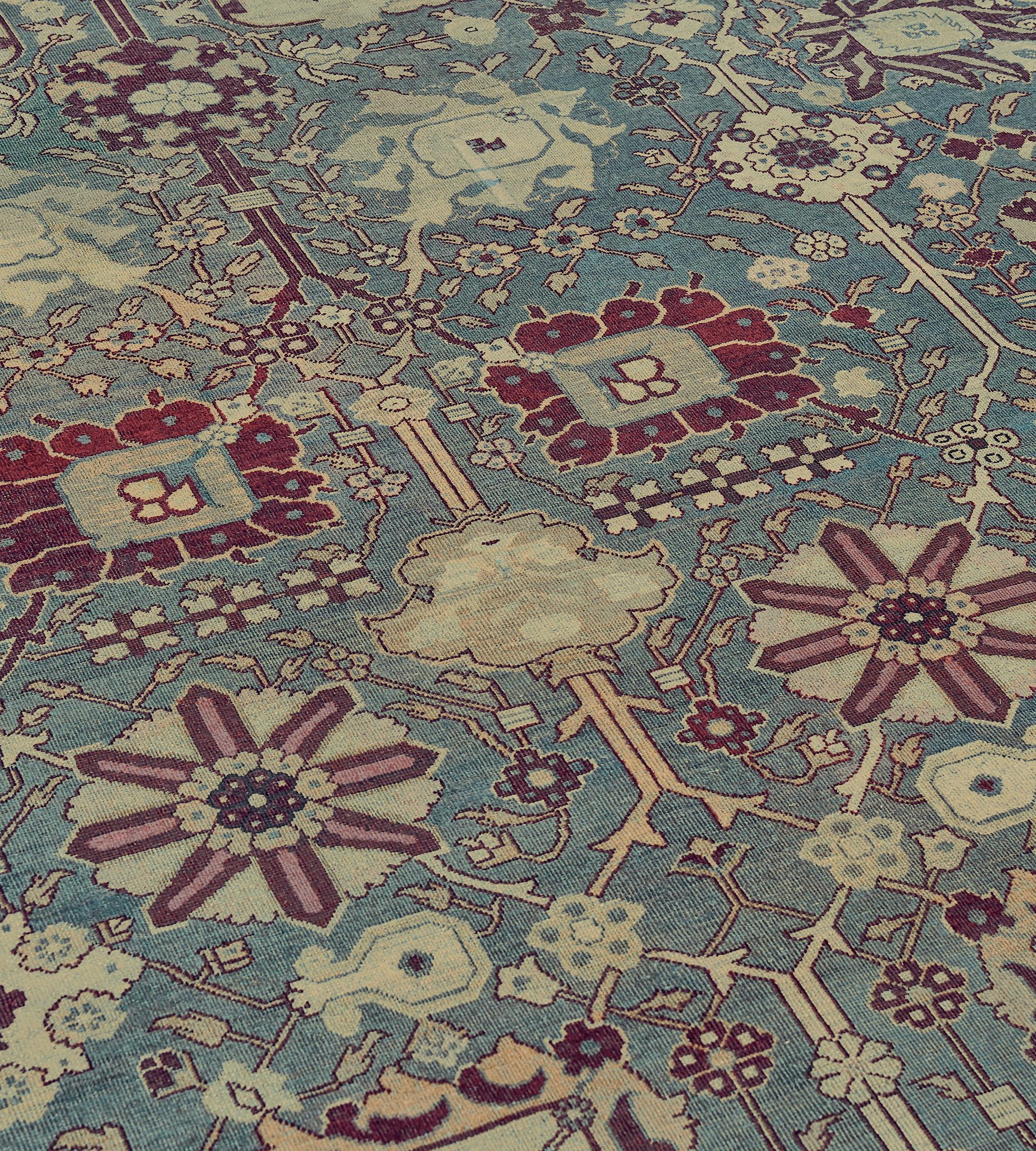 This traditional handwoven Indian Agra rug has a shaded slate field with overall counterposed design of elegant palmettes issuing scrolling angled floral vines, in a regal burgundy red border of cypress trees and flowering plants, between ornate