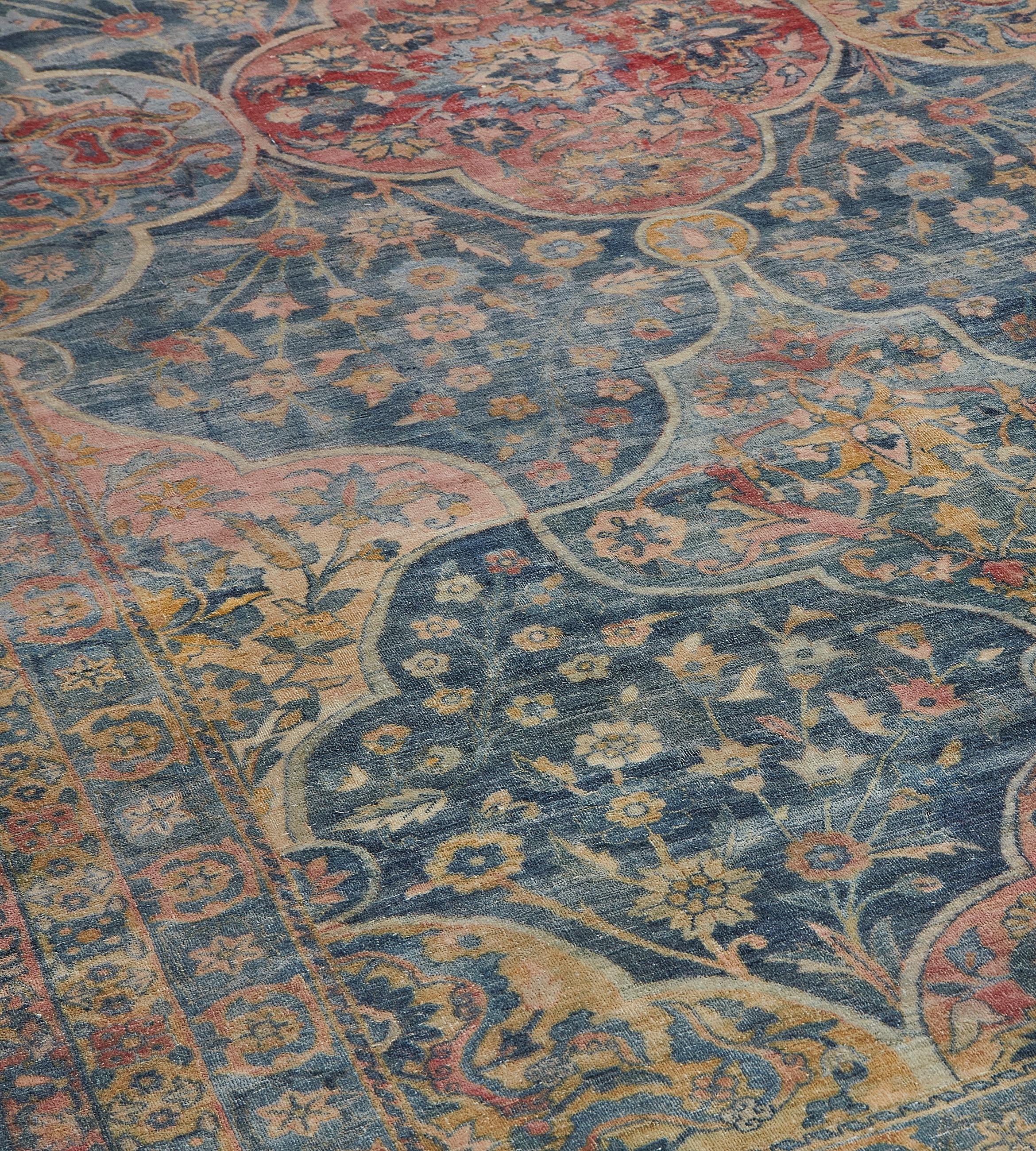 This antique Persian Kirman rug has a sea-blue field with a variety of delicate floral sprays around vertical rows of brick-red, golden-yellow and light blue palmettes alternating with cusped palmettes each containing a central flowerhead surrounded