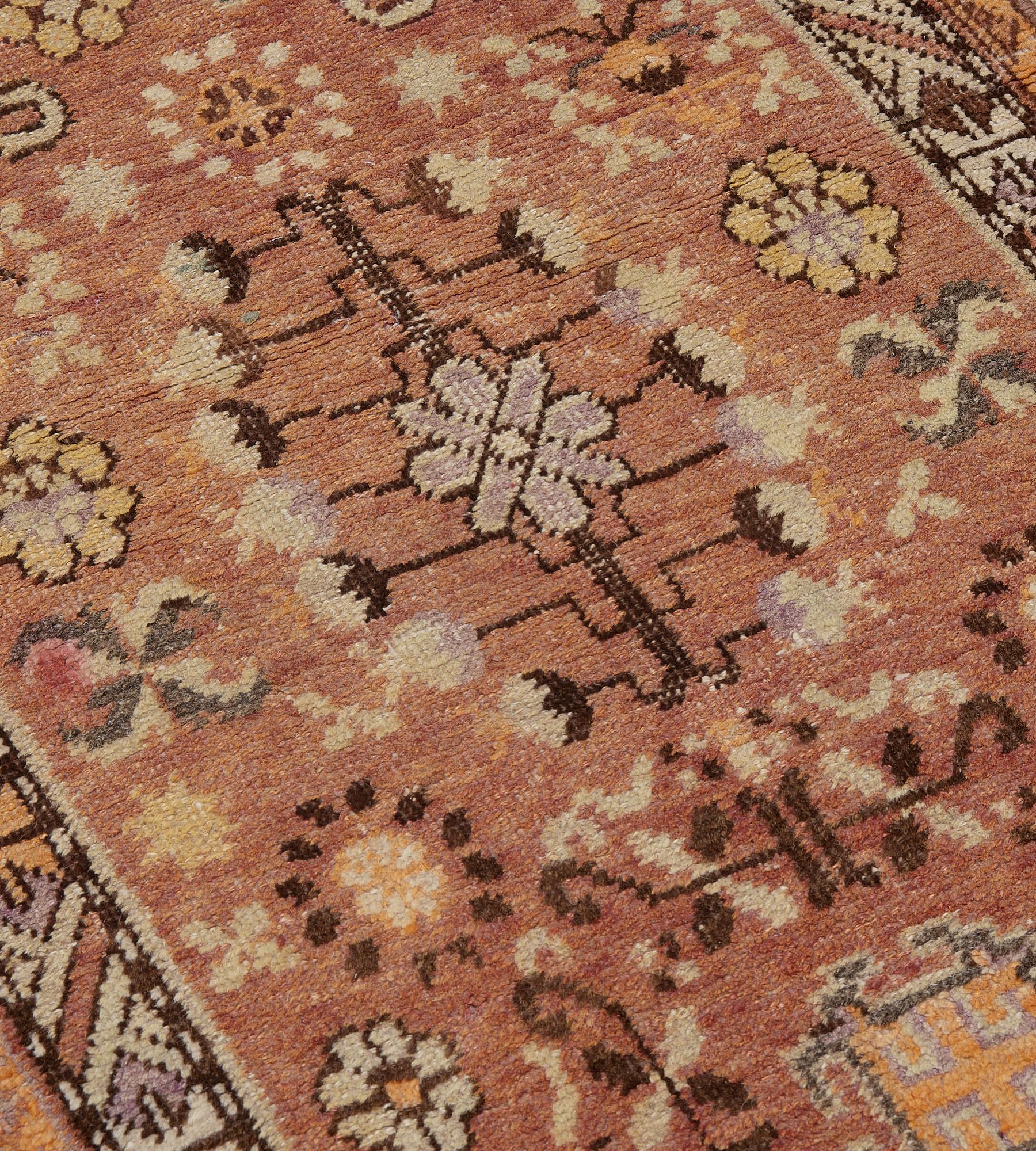 Cette ancienne coulisse Khotan, vers 1900, présente un champ brun-renard nuancé avec une colonne centrale de losanges ouverts alternés, entourés de motifs floraux et crochetés et d'autres motifs floraux et feuillus, le motif central étant entouré