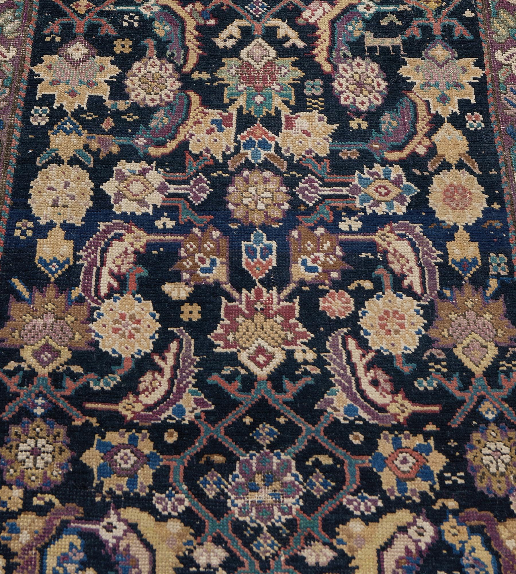 Cette antique coulisse du Karabagh présente un champ indigo avec un motif herati polychrome autour d'un losange central ivoire à gradins contenant une palmette ombrée de pourpre bordeaux et de brun sable, de petites têtes de fleurs à chaque