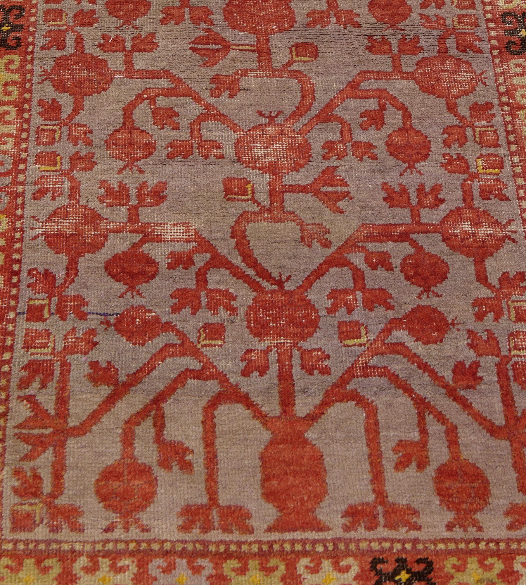 This antique, circa 1900, Khotan runner has a shaded green-grey field with an overall shaded terracotta-pink pomegranate and leafy vine, in a terracotta-pink border of golden-yellow, ivory, steel-grey and chocolate-brown hooked floral motifs between