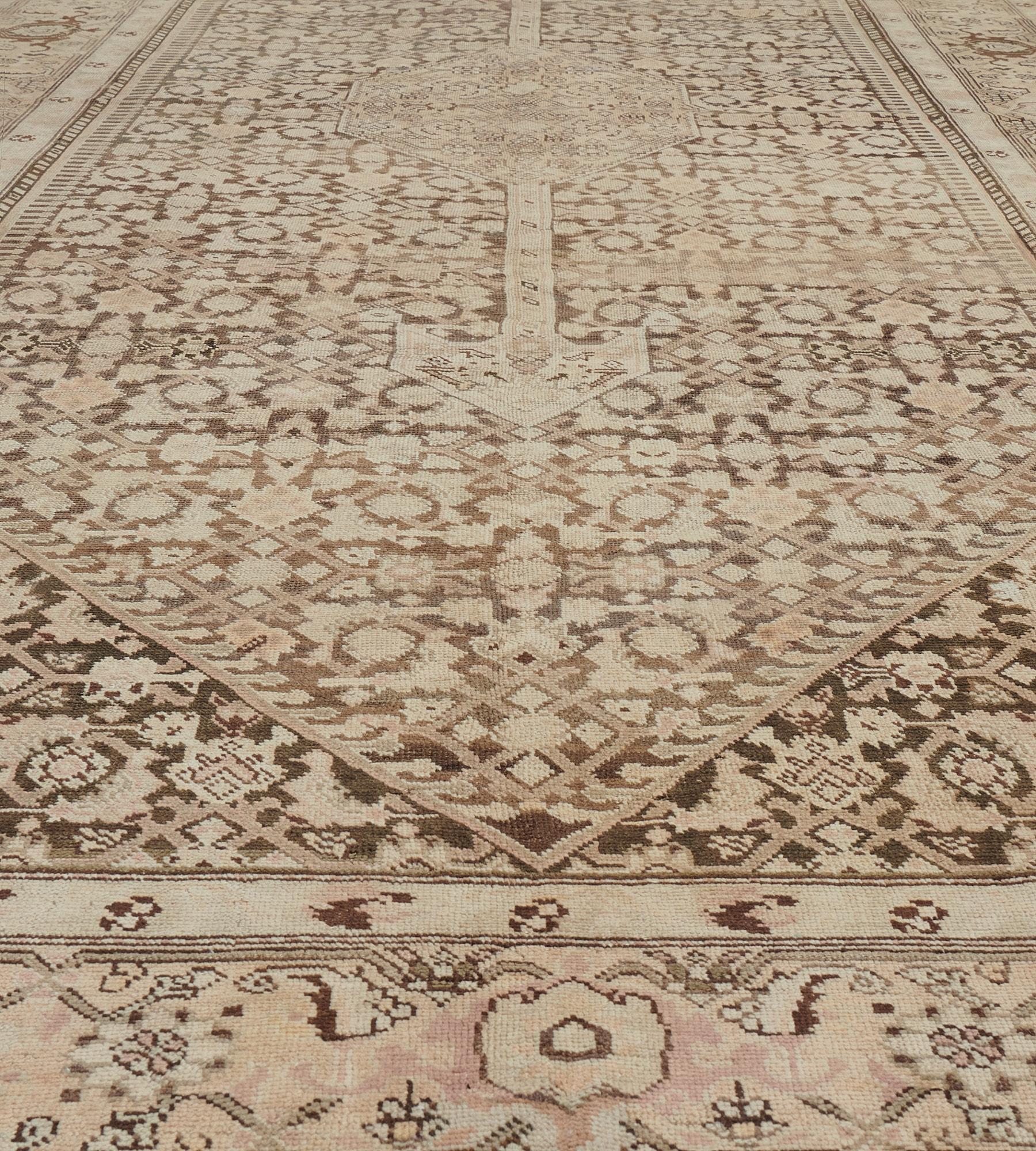 This antique Karabagh rug has a shaded brown field with a buff-brown herati-pattern around a central buff-brown lozenge medallion with palmette pendants containing a central lozenge surrounded by angular floral vine, the chocolate-brown spandrels