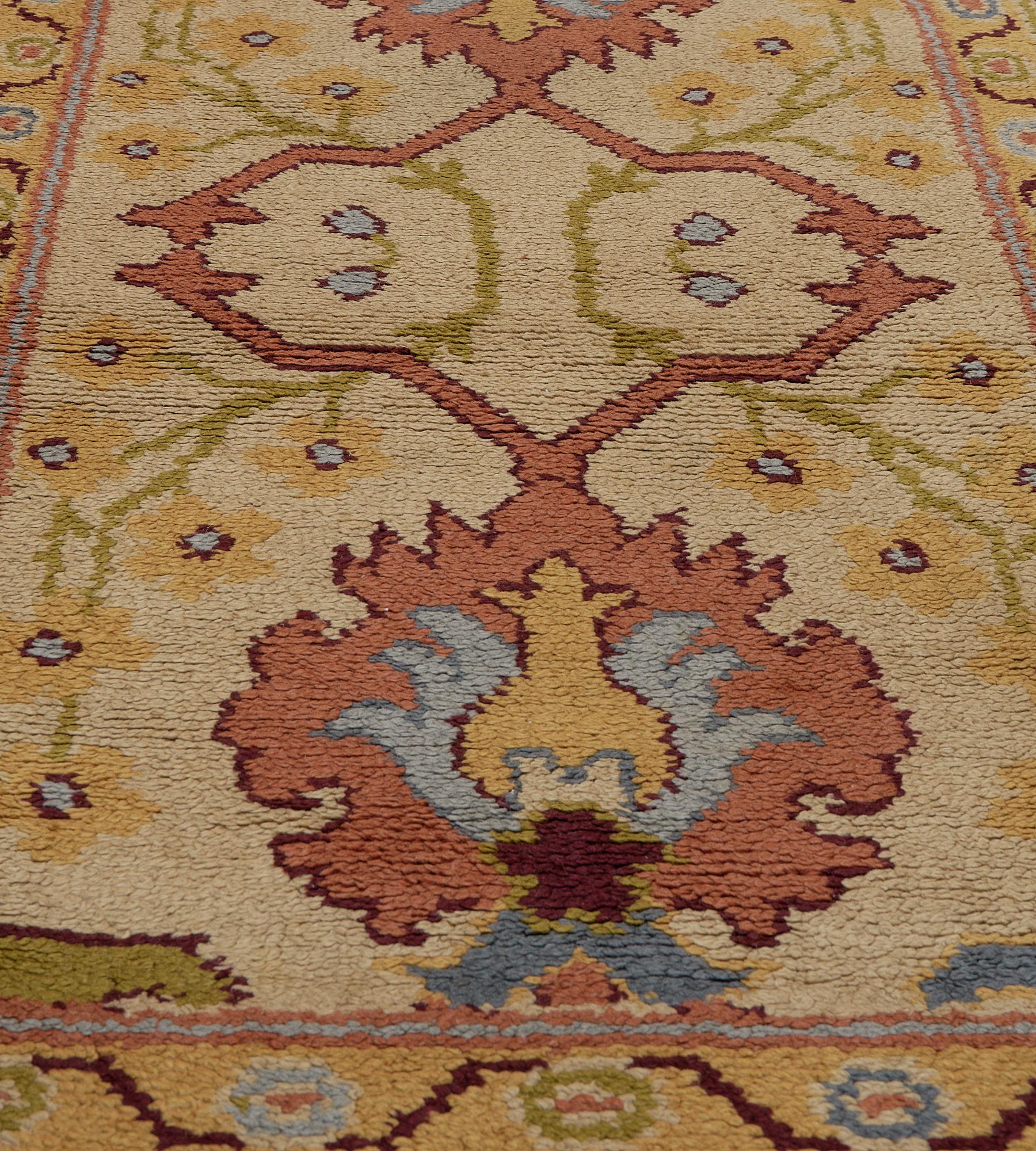 This antique, circa 1920, Irish Donegal runner has a sandy-yellow field with a column of four terracotta and light blue bold palmettes linked by angular hooked vine with a delicate moss-green scrolling vine issuing golden-yellow flowerheads a