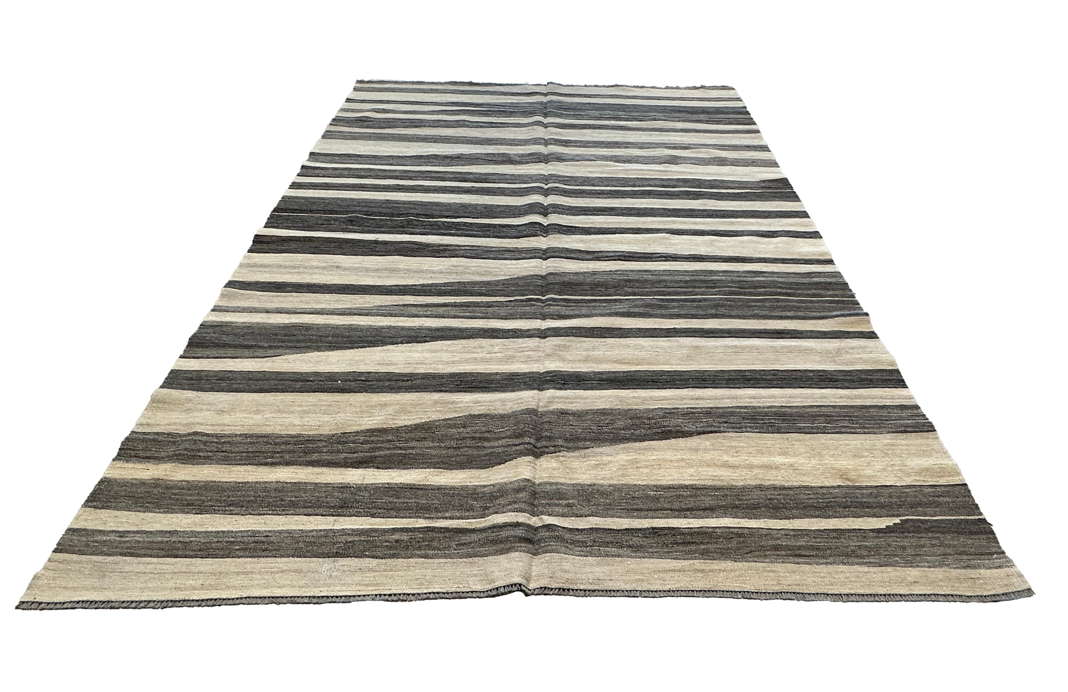 Bringen Sie mit diesem handgewebten braunen und cremefarbenen Kilim-Flachgewebeteppich ein mutiges und stilvolles Statement in Ihr Zuhause. Dieser von erfahrenen Handwerkern gefertigte Teppich zeichnet sich durch ein auffälliges Muster in satten
