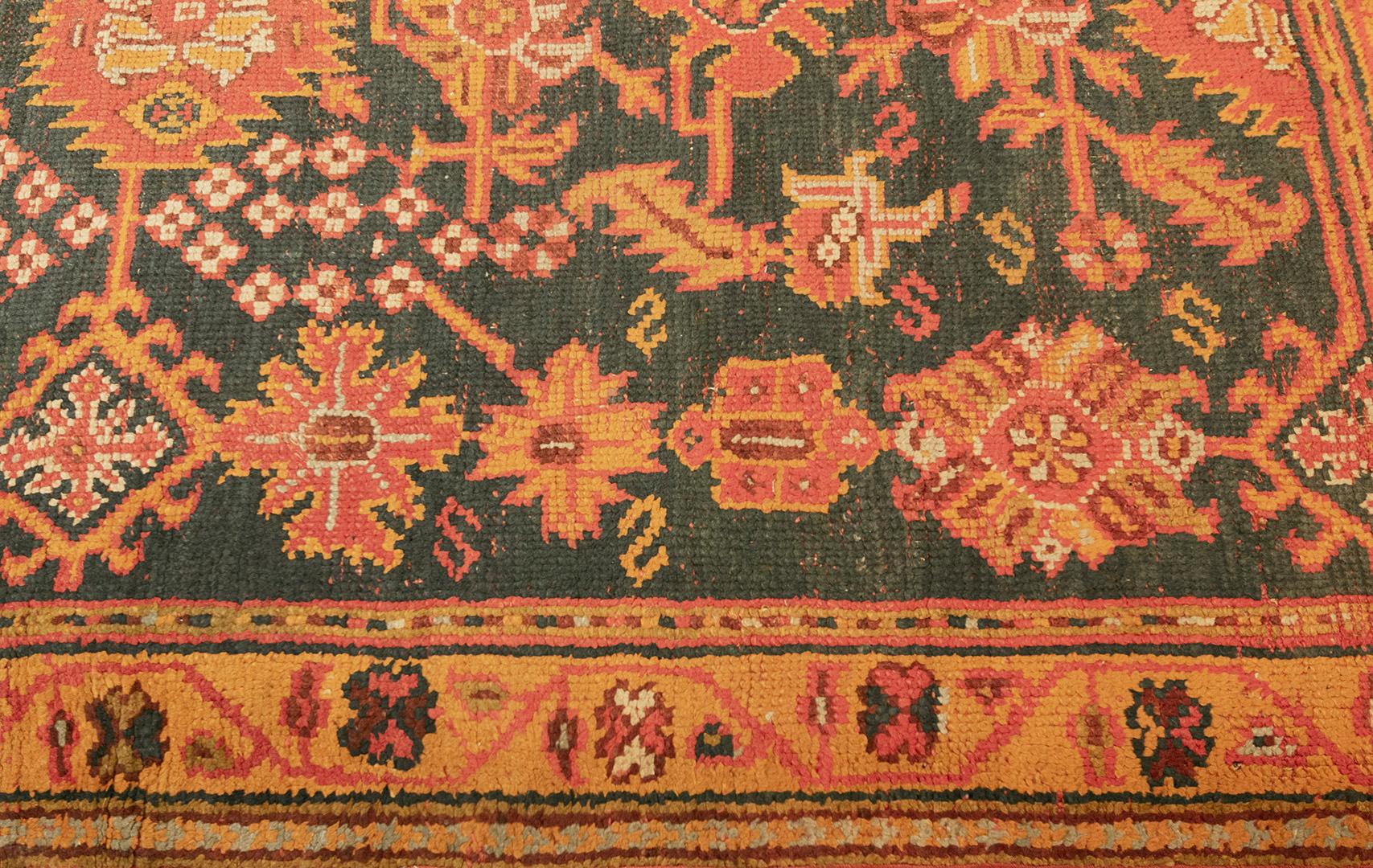 This vibrant traditional handwoven Turkish Oushak rug has an overall deep teal field with serrated palmettes and geometric floral motif linked by angled vines, in an ornate golden floral vine border, between minor geometric stripes.

Oushak (or