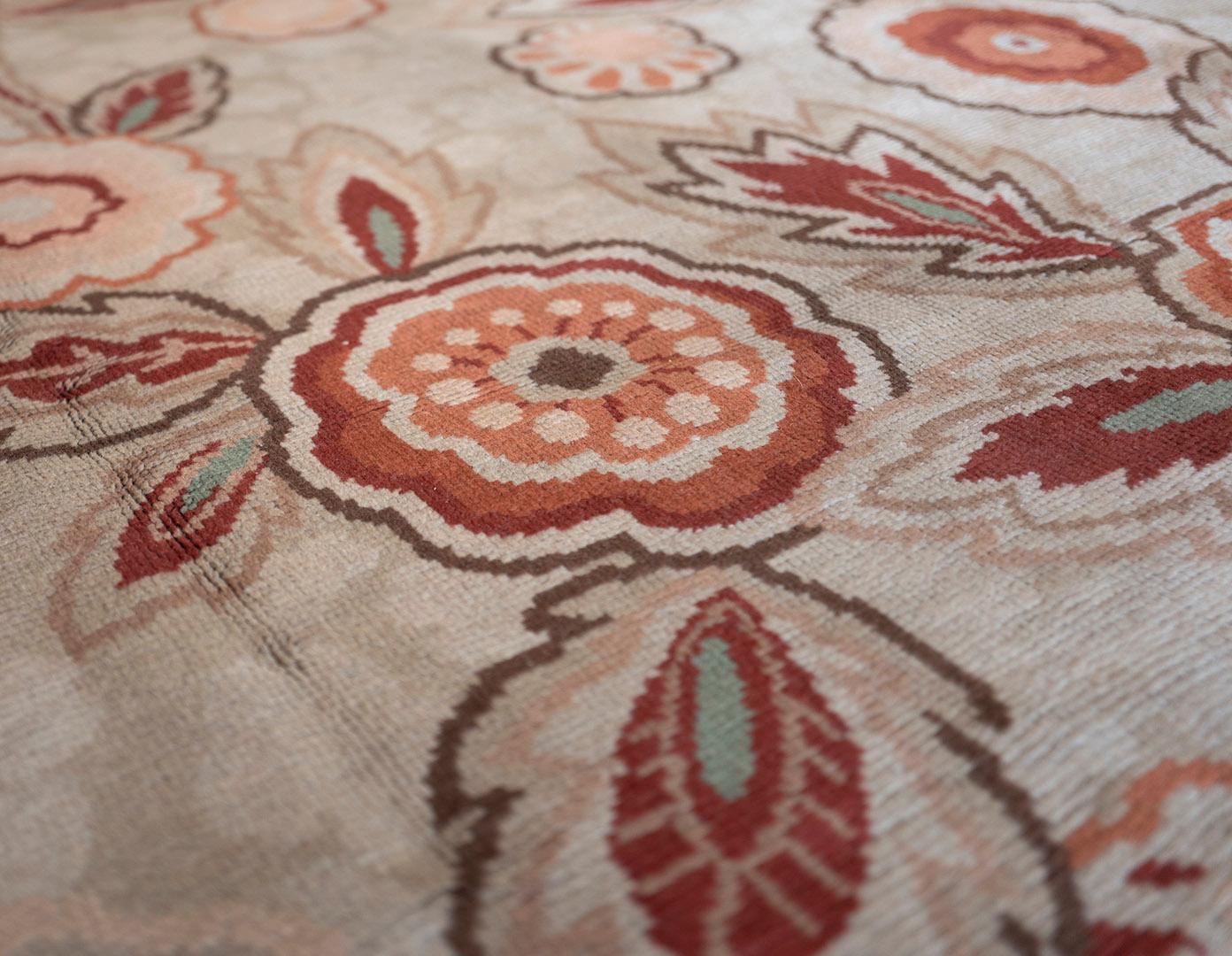 This traditional handwoven European rug has an overall taupe field and a whimsical stylized floral bouquet rendered in shades of pink and rust, in a brown border.