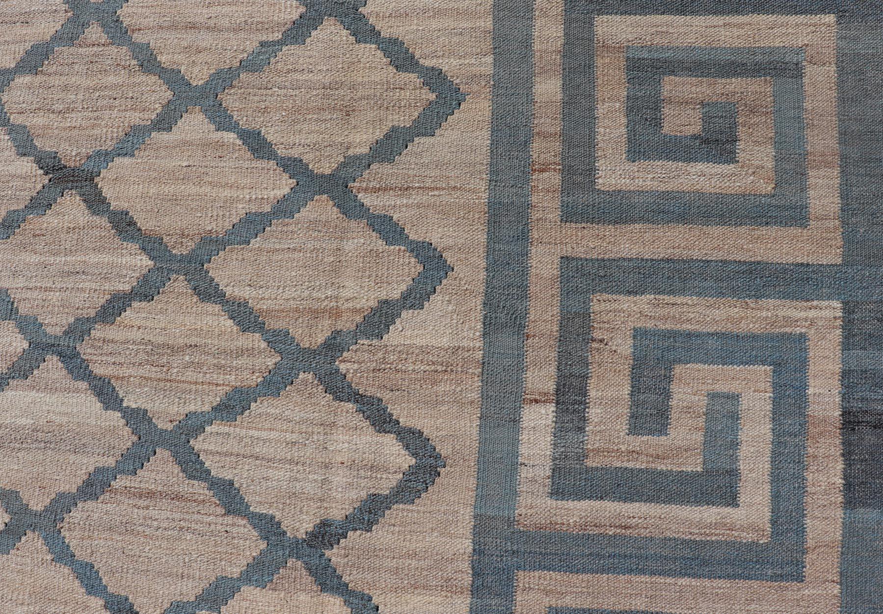 This flat-weave kilim has been hand-woven. The rug features a modern diamond design, enclosed within a Greek key border. The rug is rendered in blue, gray and earthy tones, making this rug a superb fit for a variety of classic, modern, casual and