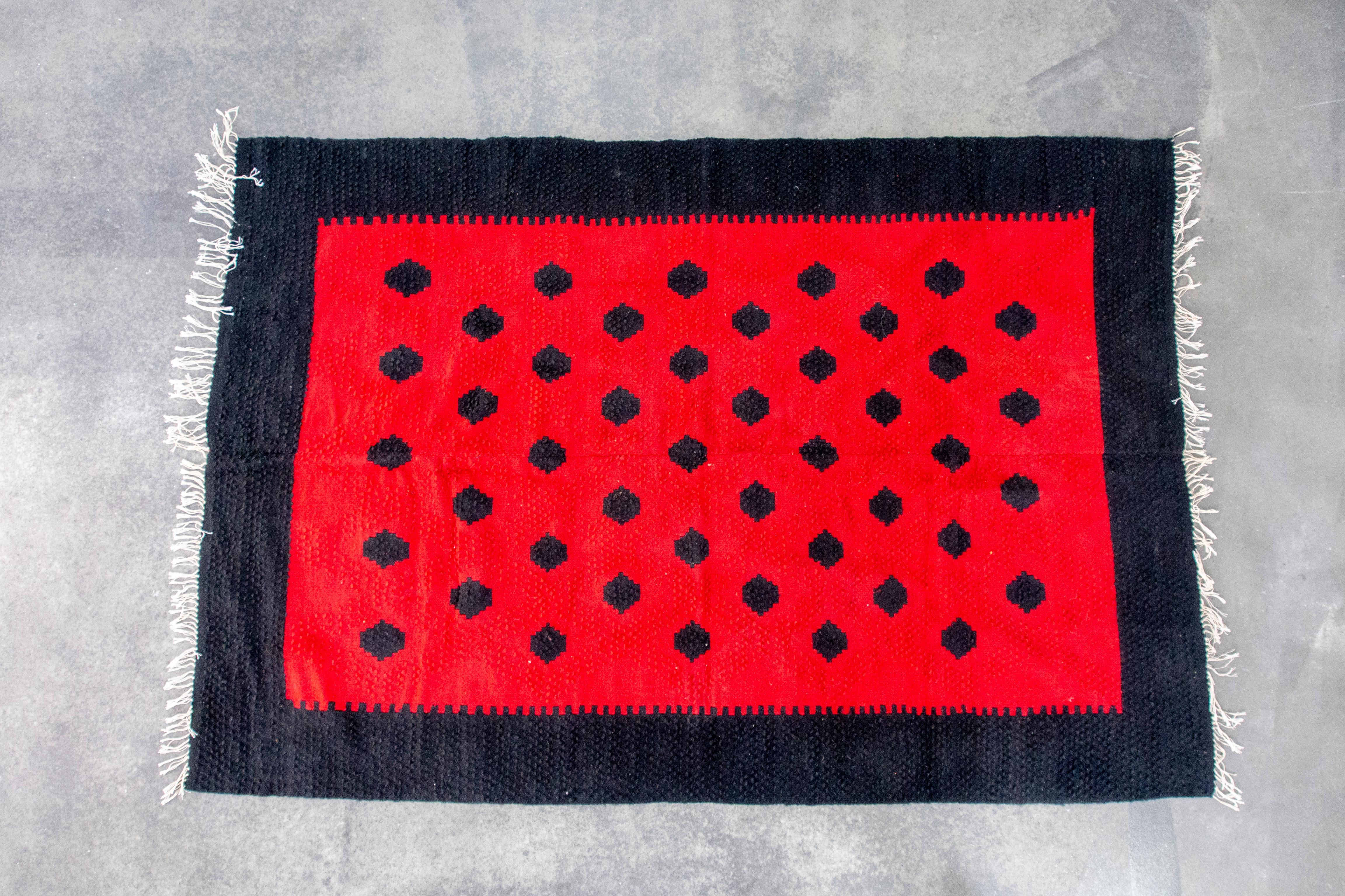 In this listing you will find a beautiful hand-woven kilim in red and black wool. It features geometrical pattern, inspired by a watermelon or ladybug. Vibrant red in stark contrast with black makes for a very attractive piece of decor for your